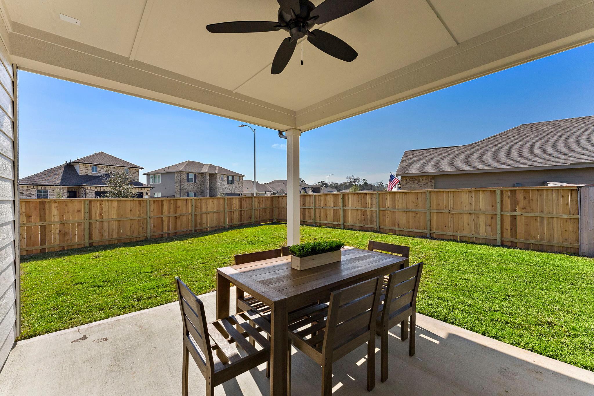 Covered patio at Sundance Cove in Crosby Texas with wooden dining table, chairs, ceiling fan, green lawn and privacy fence