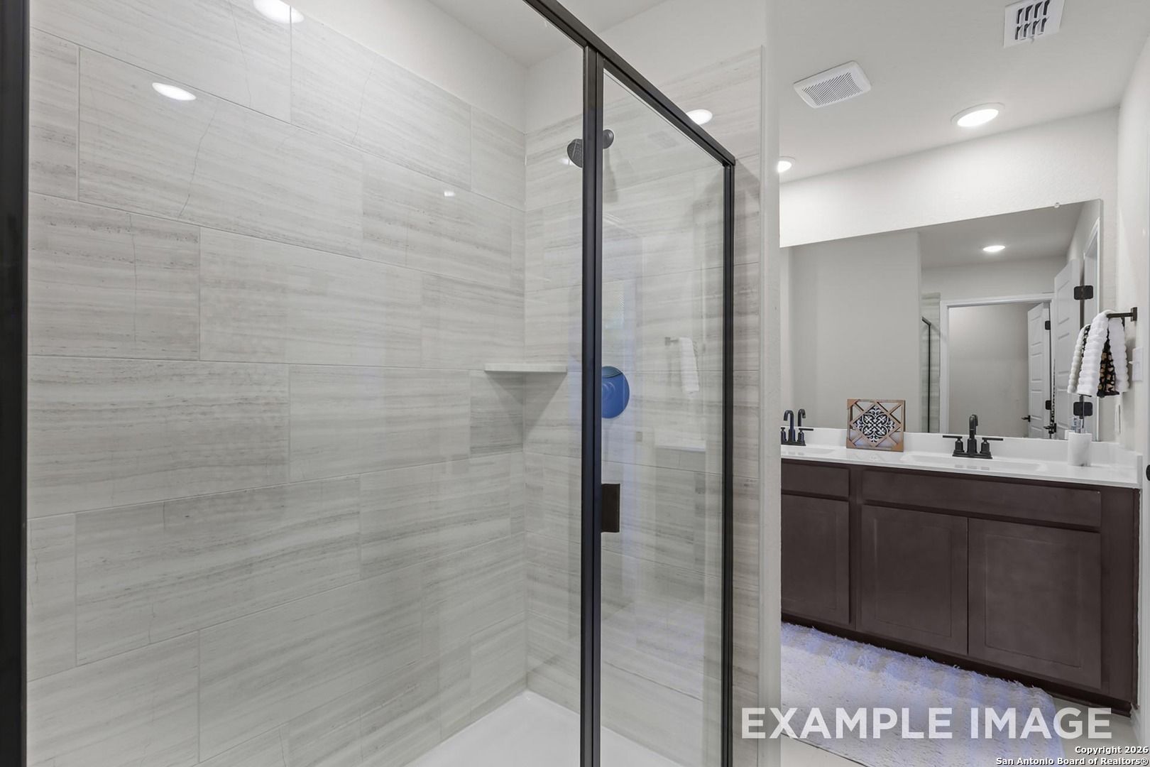 Elegant master bathroom with gray subway tile, frameless glass shower, and double vanity in Davidson Homes Trinity B, San Antonio