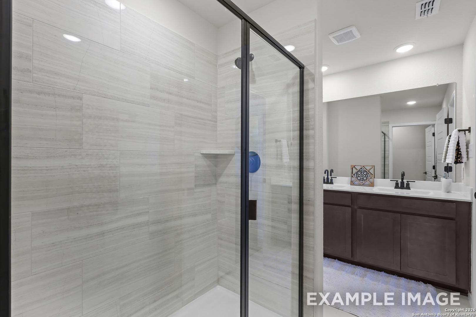 Elegant master bathroom with gray subway tile, frameless glass shower, and double vanity in Davidson Homes Trinity B, San Antonio