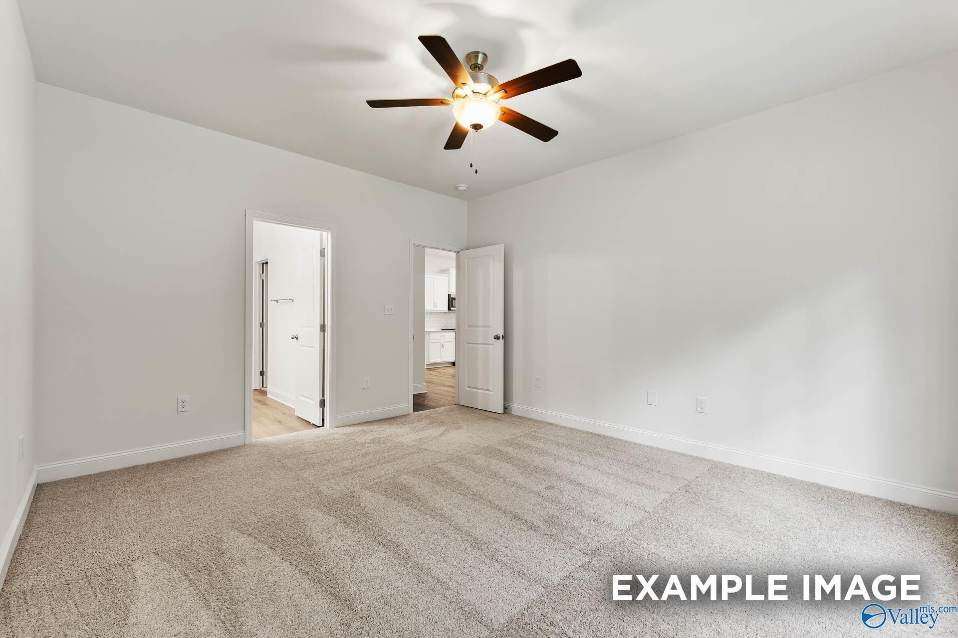 Spacious empty bedroom with ceiling fan, white walls, beige carpet, and doors to bathroom in Davidson Homes The Daphne V, Athens, Alabama