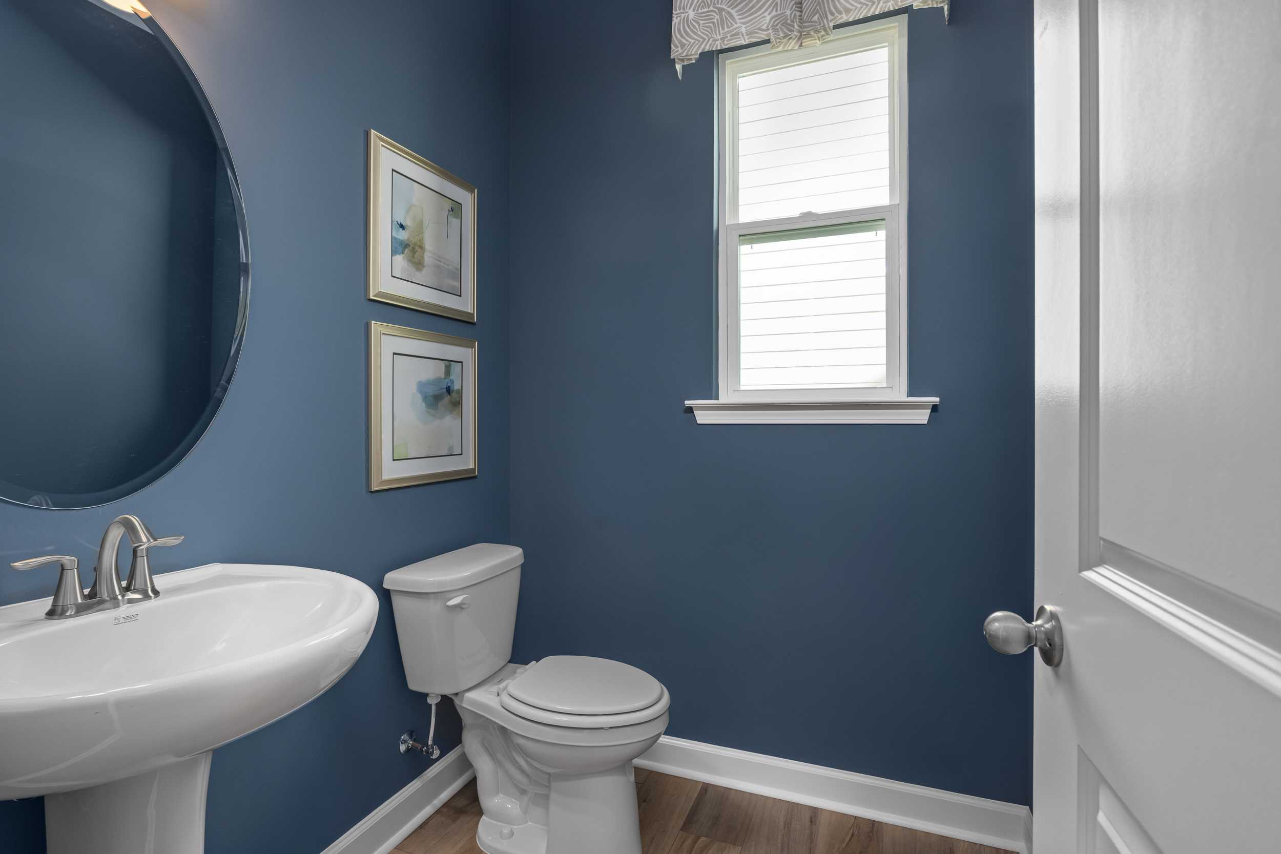 Navy blue powder room in The Hickory II E by Davidson Homes featuring round mirror, framed art, white sink, and toilet