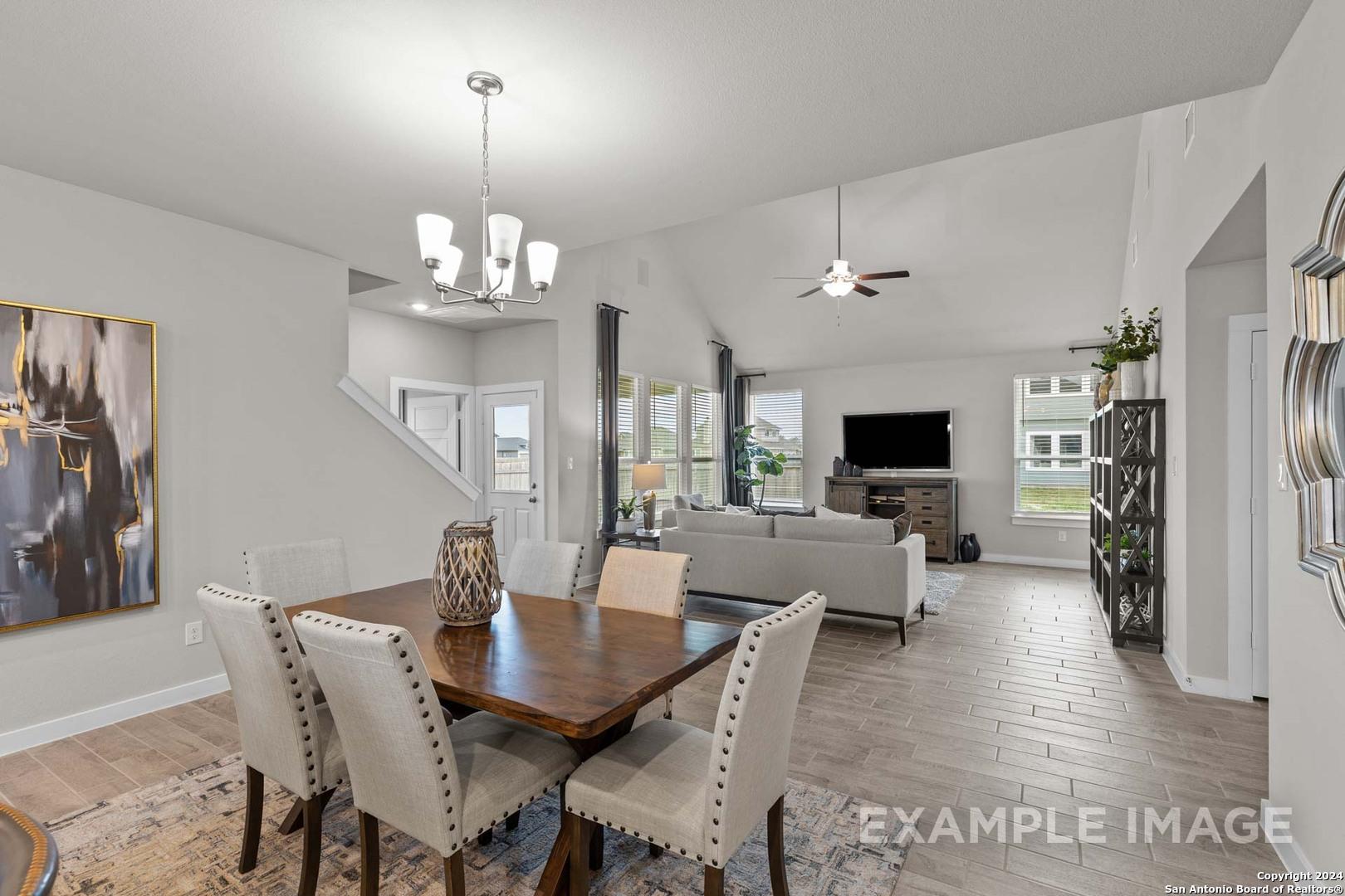 Open-concept living-dining area with wooden table, beige sofa, chandelier, and large windows in Davidson Homes The Collin A, Seguin, Texas