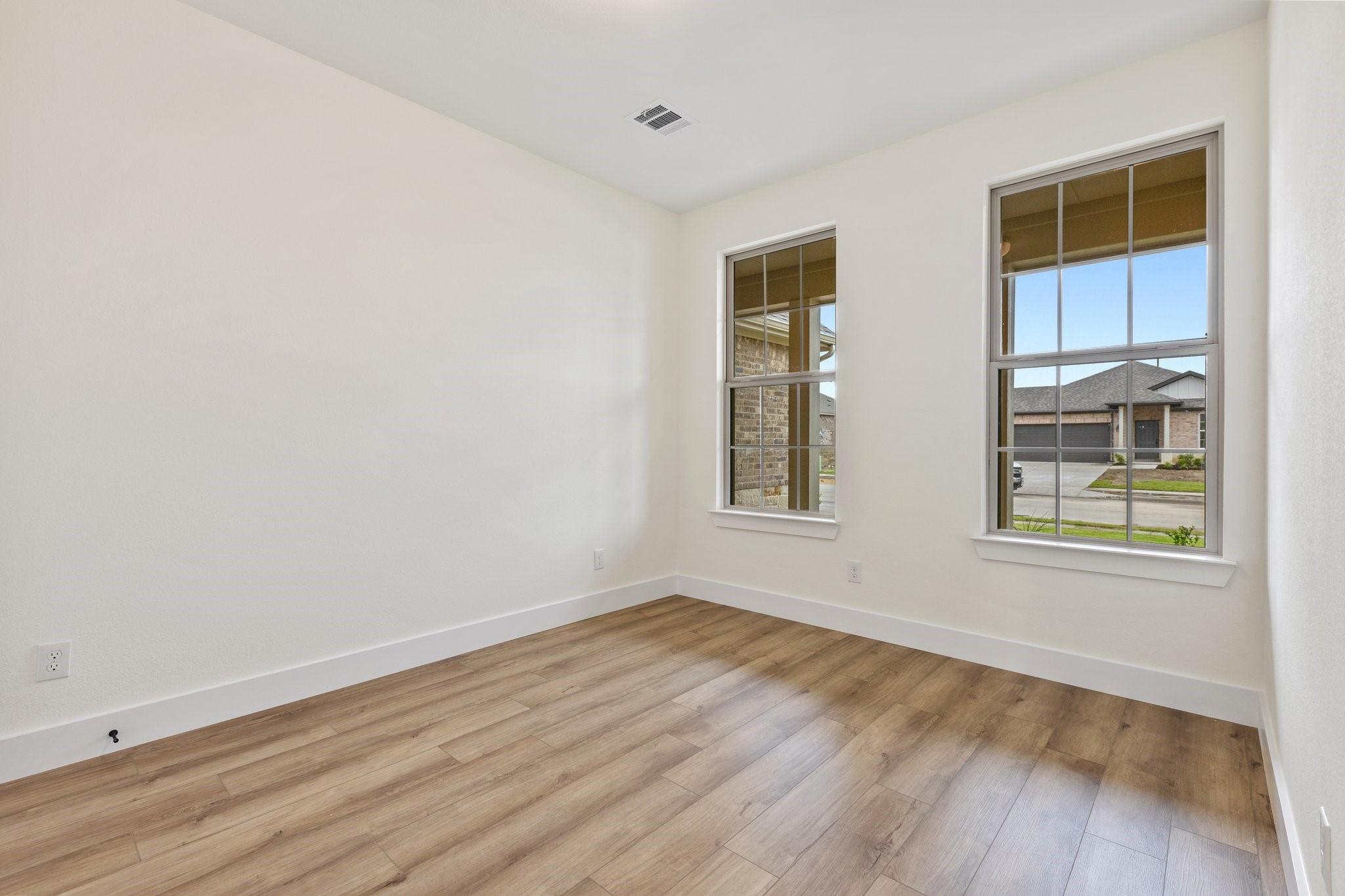 Bright, unfurnished bedroom with wood-look flooring in The Rockford C floor plan at Waverly Estates in Josephine, Texas.