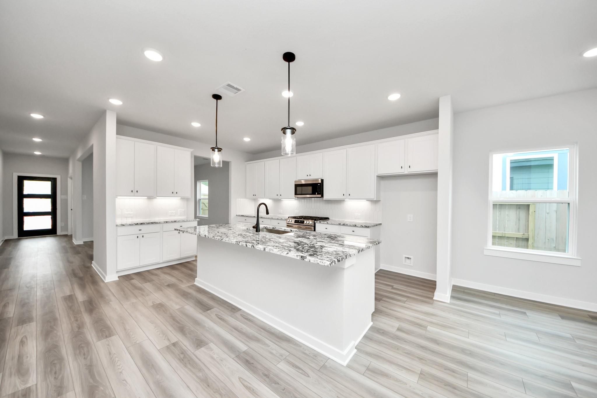 Modern kitchen with granite island and white cabinets in The Sorrento E floor plan at Sundance Cove, Crosby, Texas.