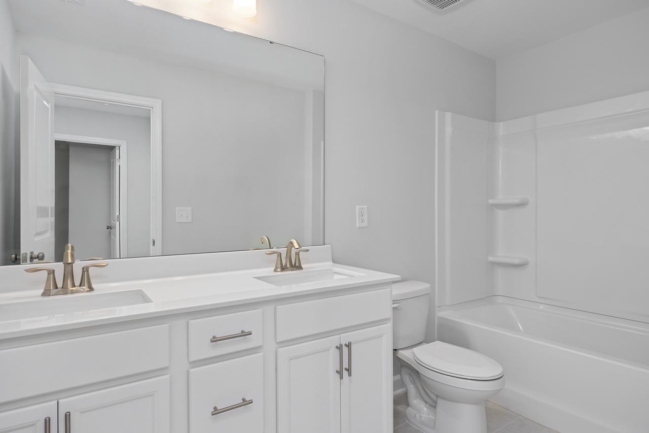 Spacious master bathroom in The Durham C with dual white vanities, gold faucets, large mirror, soaking tub, and shower