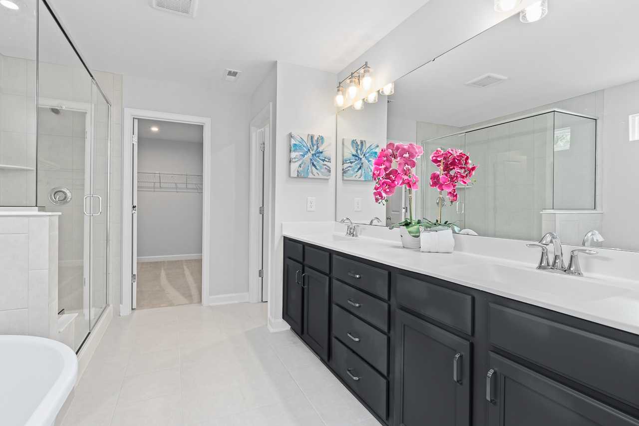 Spacious primary bathroom at Stagecoach Corner in Mebane NC with frameless glass shower, black double vanity, orchids