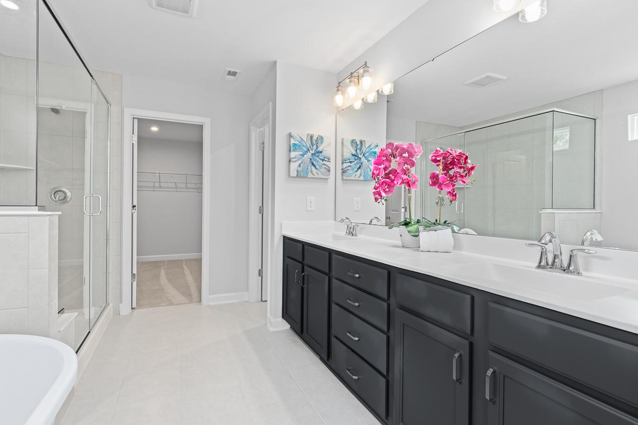 Spacious primary bathroom at Stagecoach Corner in Mebane NC with frameless glass shower, black double vanity, orchids