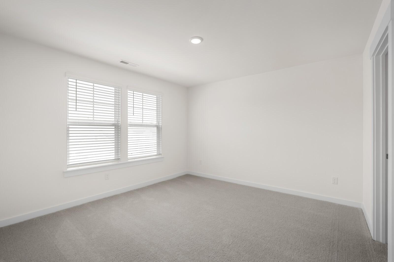 Bright, neutral bedroom with plush carpet and windows in The Willow floor plan by Davidson Homes in Gallatin, Tennessee.
