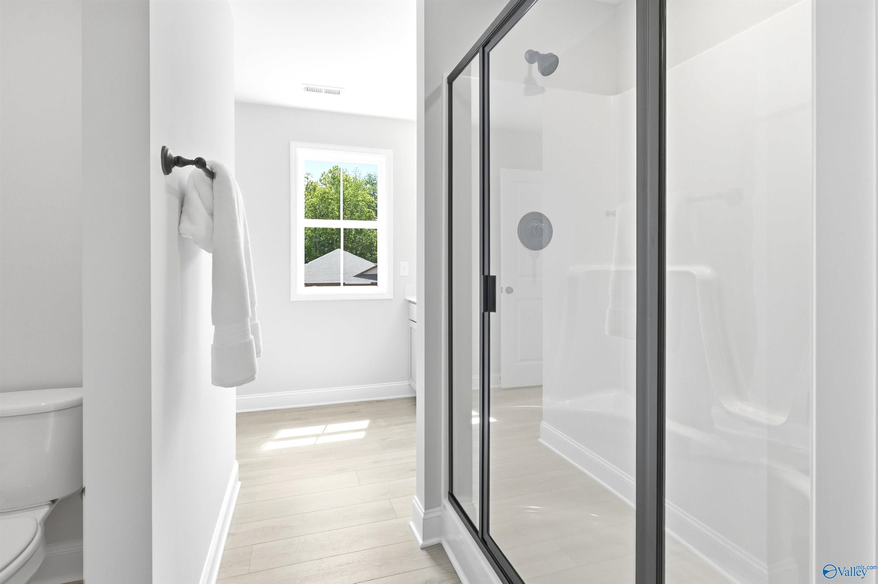 Bright white bathroom with black-framed glass shower, towel rack, and window view in Davidson Homes The Russell A, Huntsville