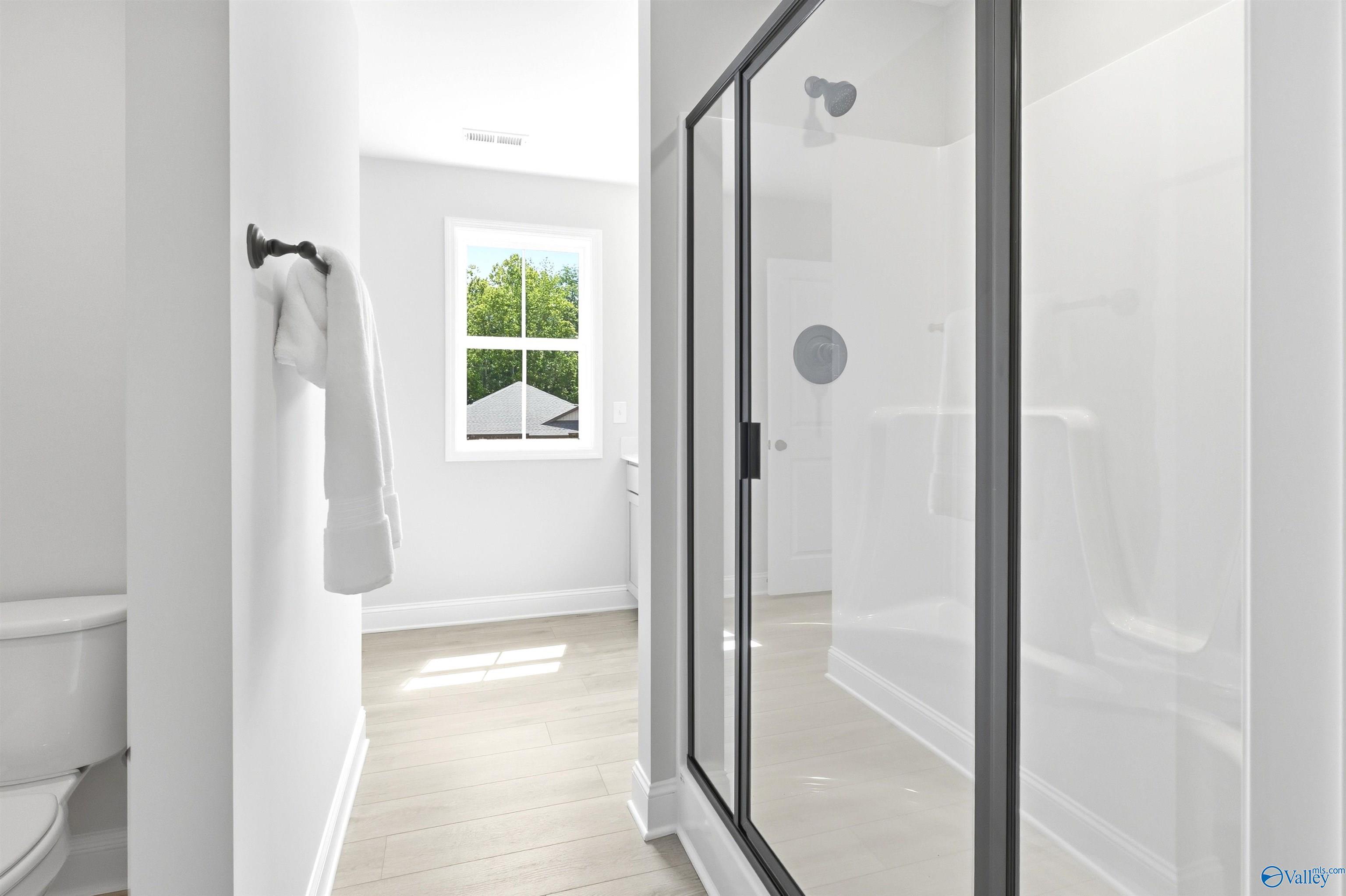 Bright white bathroom with black-framed glass shower, towel rack, and window view in Davidson Homes The Russell A, Huntsville