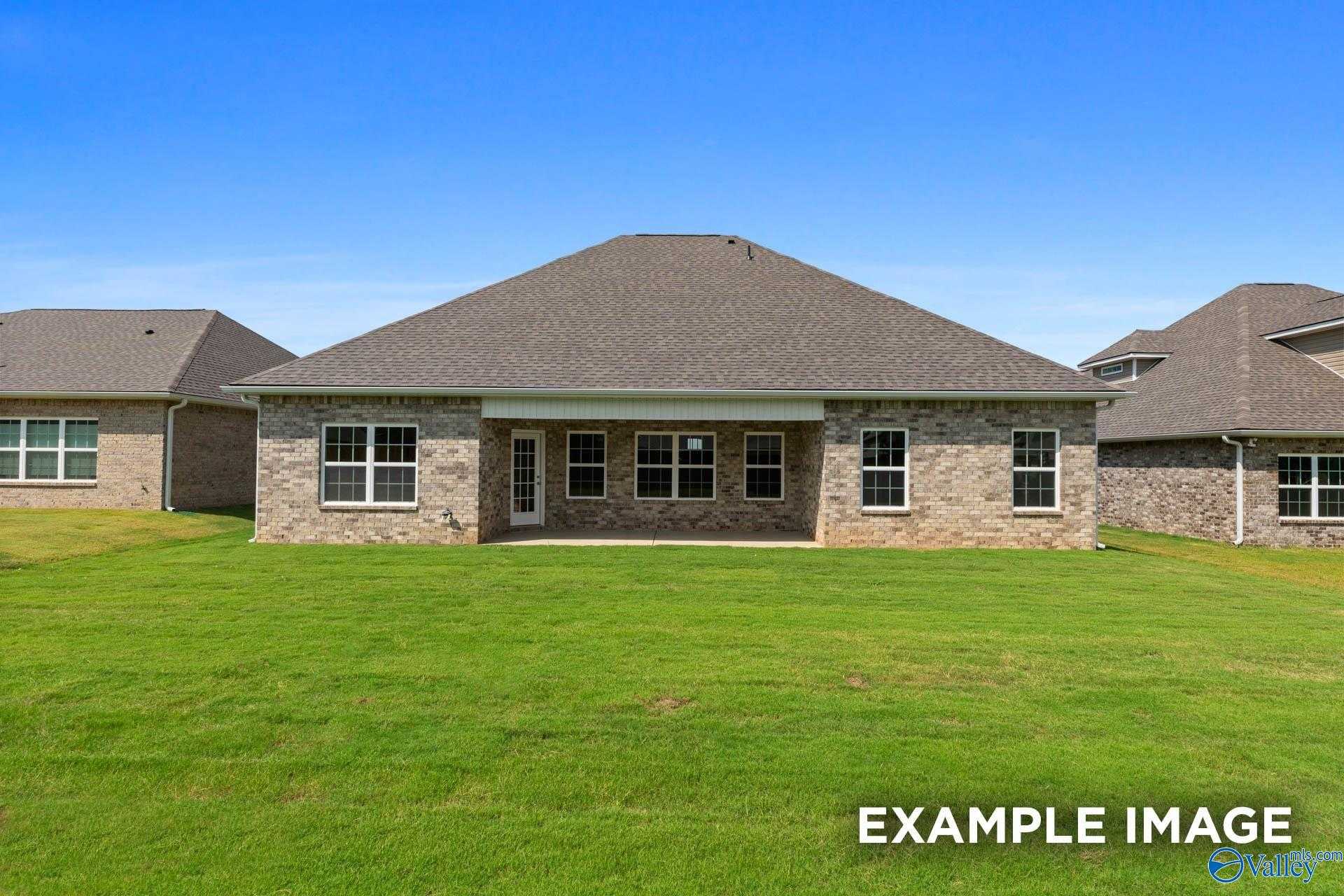 Rear view of single-story brick home with covered patio, large windows, and green yard in The Meadows, Athens, Alabama