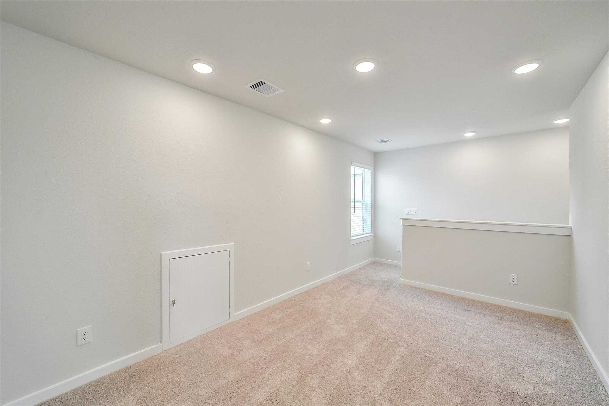 Bright upstairs loft with beige carpet, railing, large window, and recessed lights in Davidson Homes The Blanco E, Magnolia, Texas