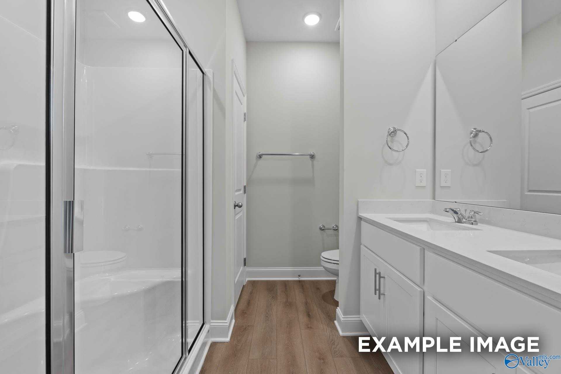 Modern master bathroom featuring glass shower, double vanity sinks, and luxury wood flooring in Davidson Homes The Butler, Huntsville AL