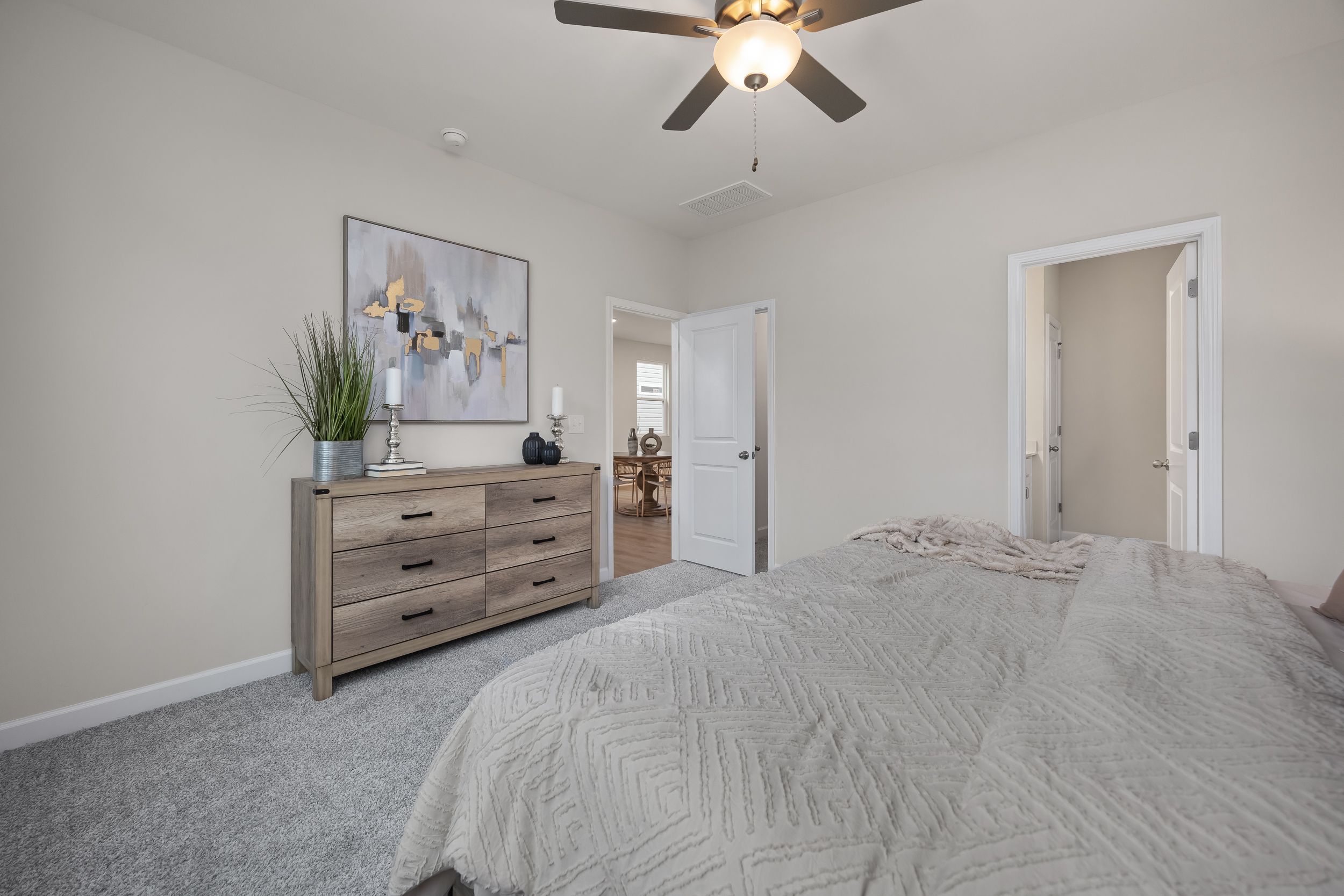 Spacious bedroom at Gregory Village in Lillington, NC by Davidson Homes featuring a wooden dresser and ceiling fan.