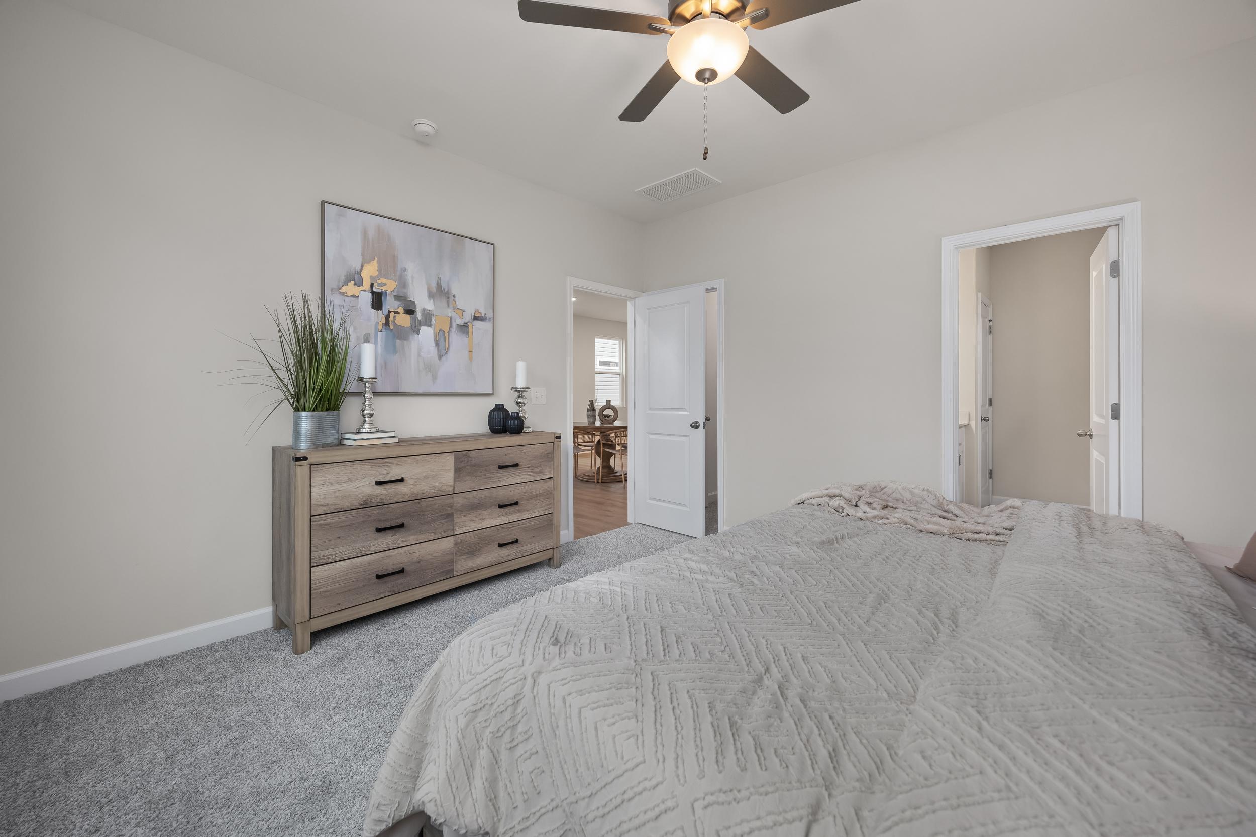 Spacious bedroom at Gregory Village in Lillington, NC by Davidson Homes featuring a wooden dresser and ceiling fan.