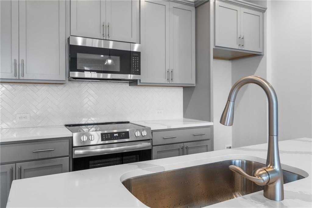 Modern kitchen with white subway tile backsplash, stainless steel microwave and range, quartz counters, gray cabinets in The Monroe A, Emerson, GA