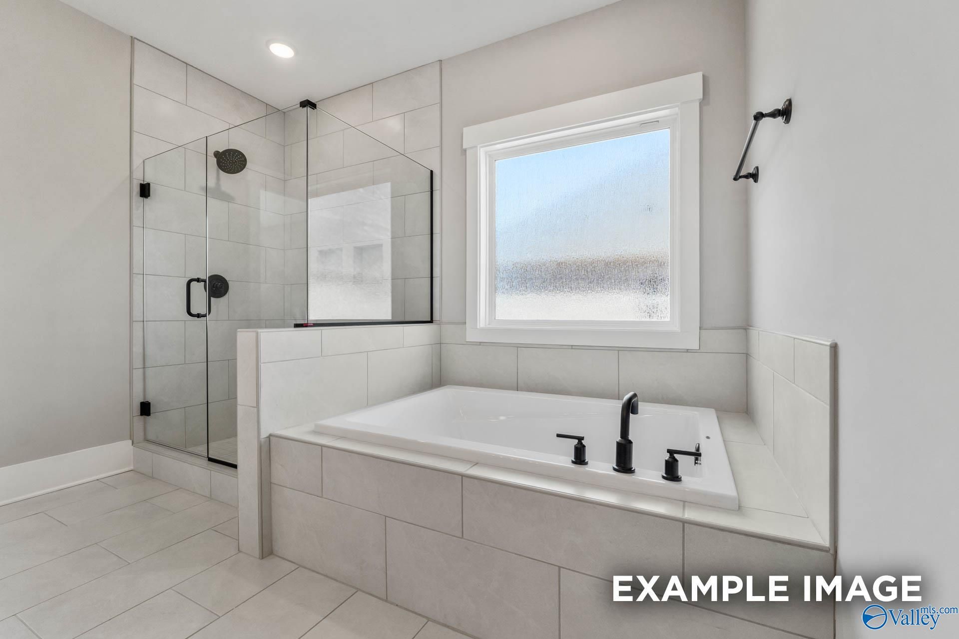 Modern primary bathroom with soaking tub, glass-enclosed shower, and tile surround in The Finleigh, Briercreek, Meridianville.