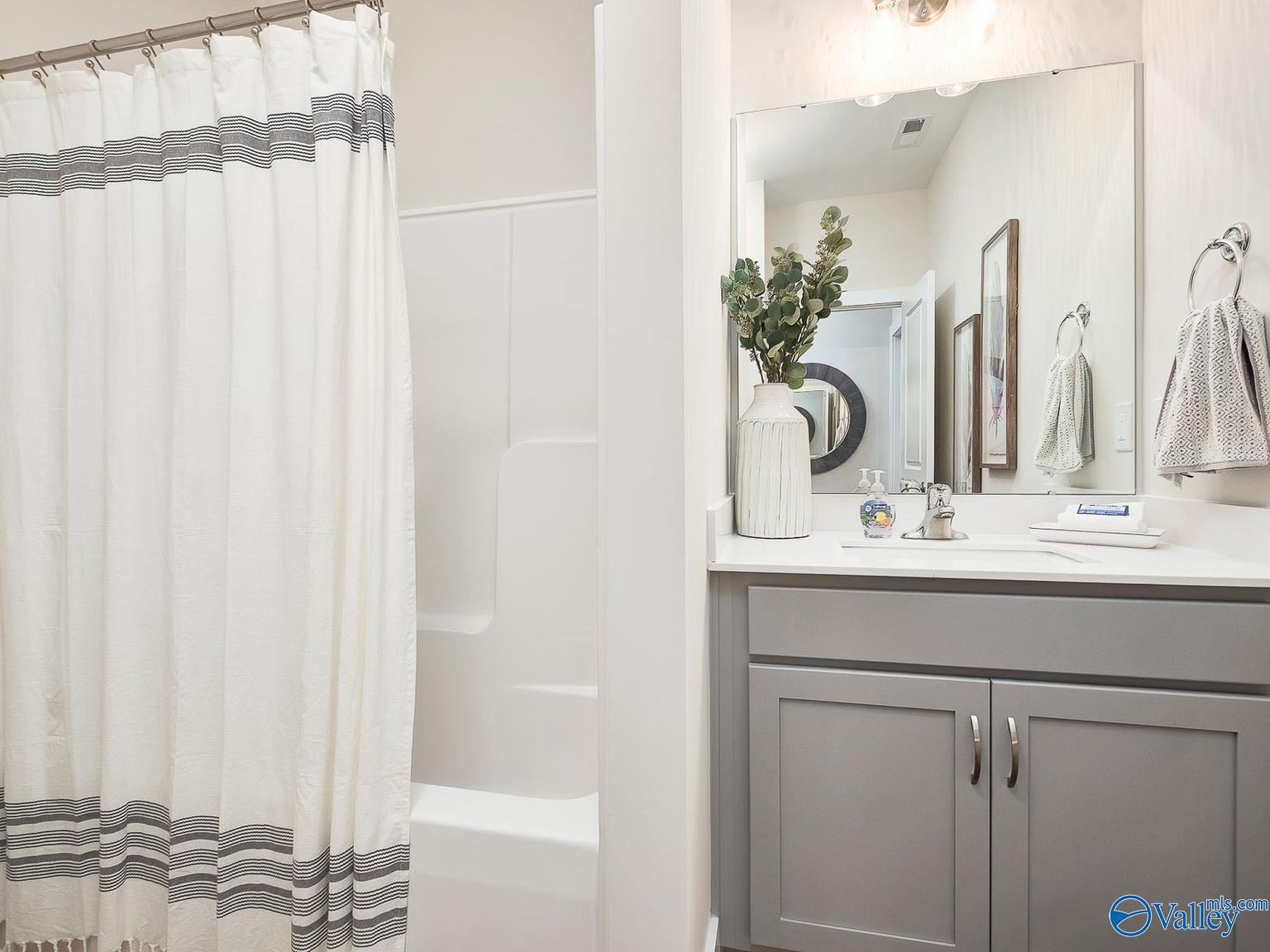 Modern bathroom featuring gray double vanity, white subway tile shower with striped curtain in Davidson Homes Everett, Toney AL