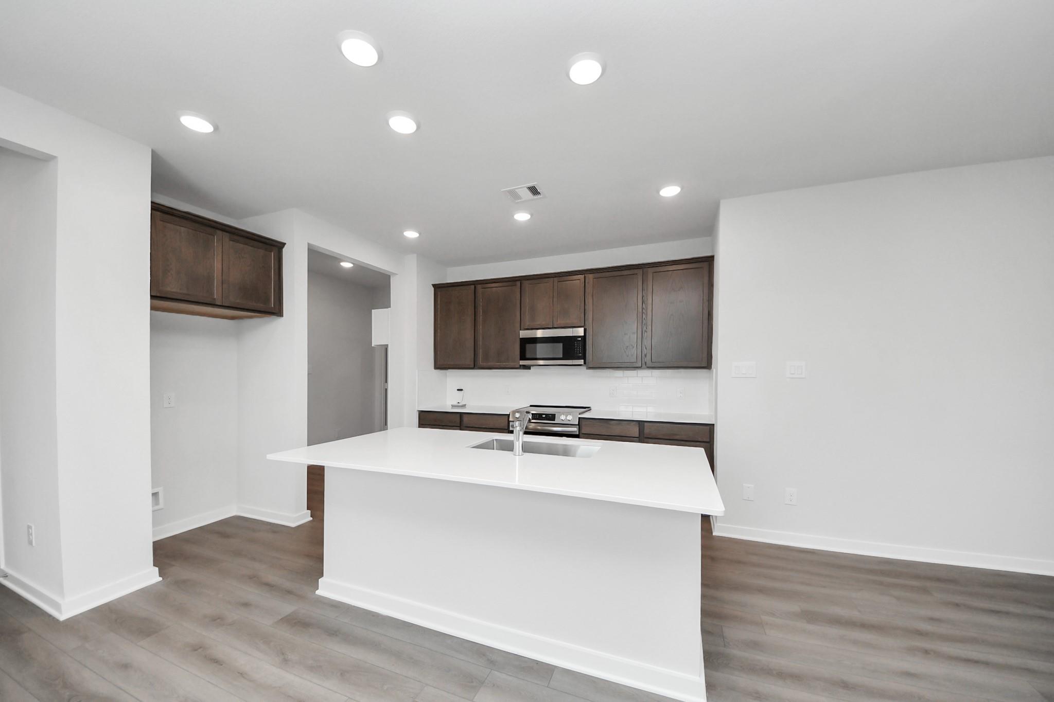 Modern kitchen with white island, dark wood cabinets, and stainless steel appliances in The Brazos F, Liberty Estates home.