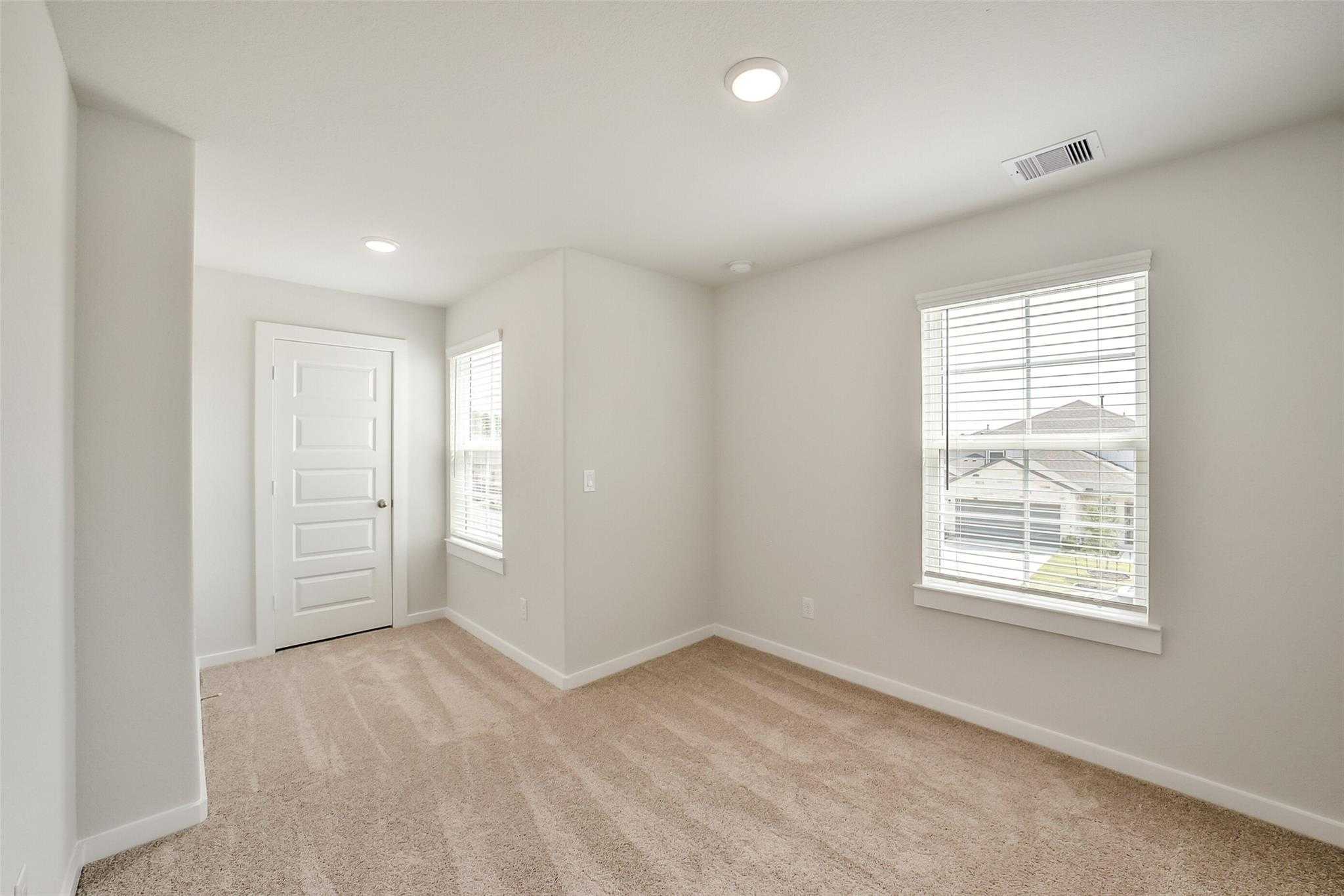 Cozy secondary bedroom featuring beige walls, tan carpet, and window with blinds in Davidson Homes The Blanco E, Magnolia, Texas