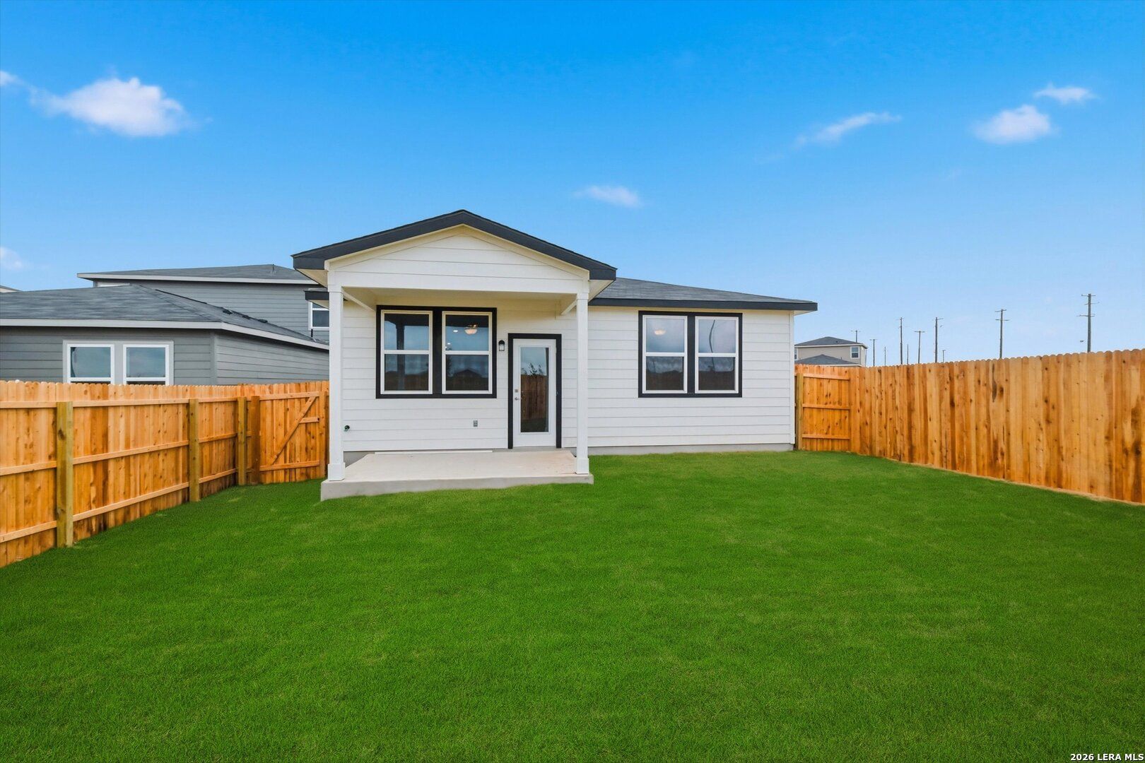 Back view of The Frio B single-story home featuring covered patio, large windows, and fenced green backyard in Agave, San Antonio, Texas