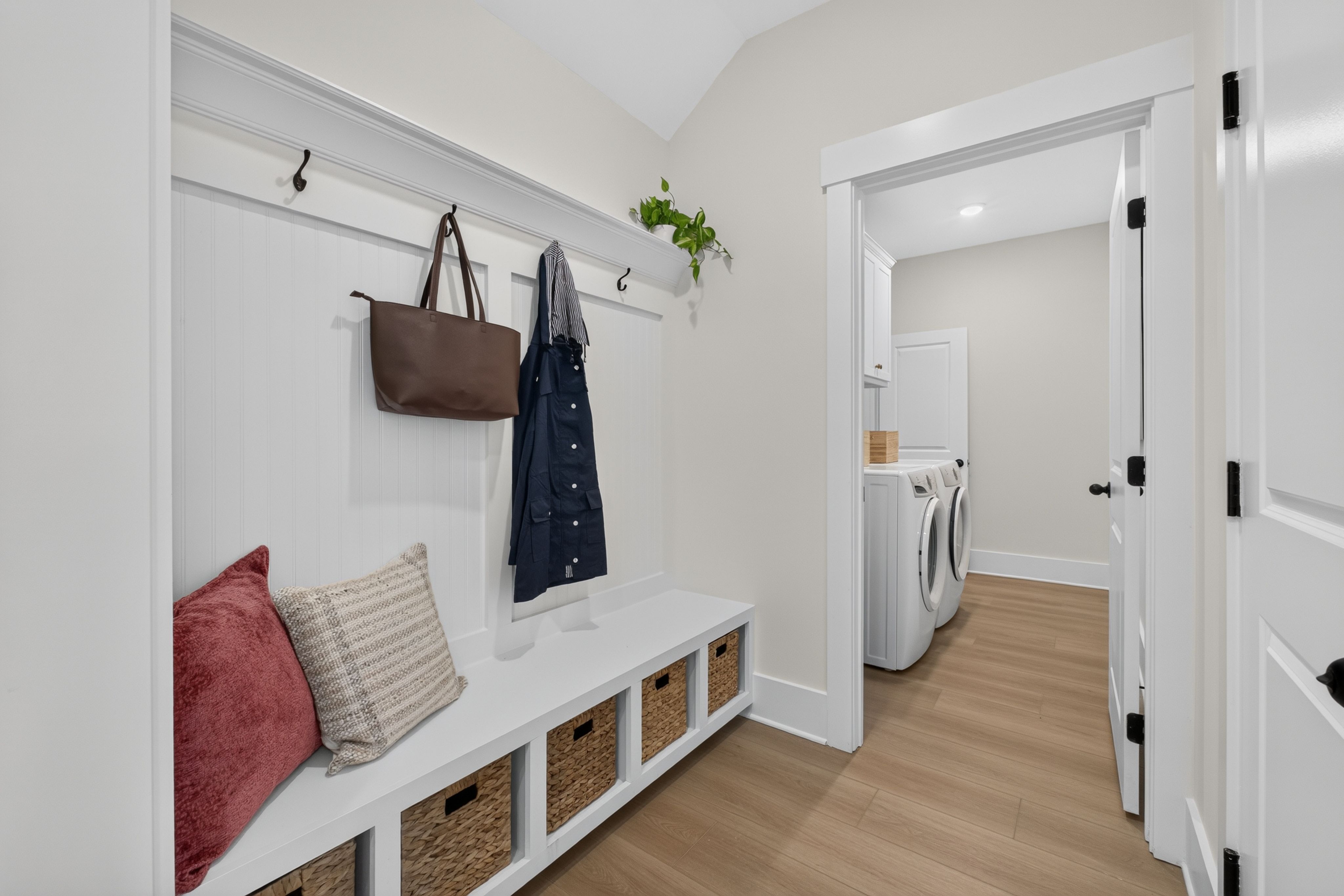 White mudroom with built-in bench, storage baskets, and coat hooks at Evergreen Mill by Davidson Homes in Madison, AL
