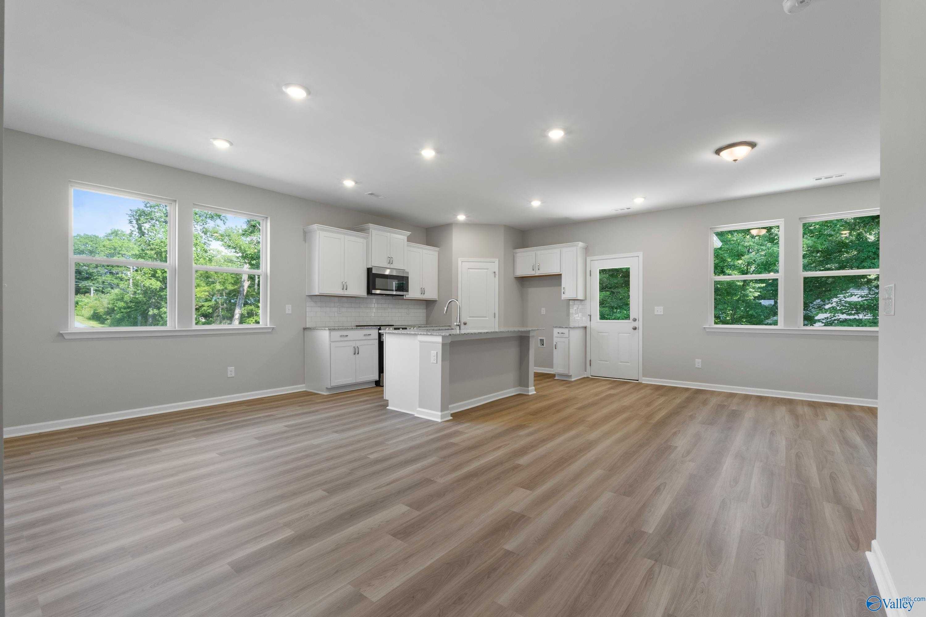 Modern open kitchen with white shaker cabinets, granite island sink, and lush window views in The Polaris 3-bedroom home, Fayetteville, TN