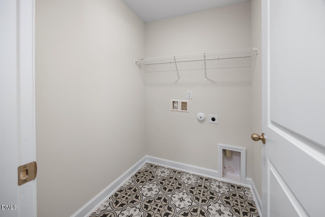 Spacious laundry room featuring wire shelving, washer-dryer hookups, pet door, and patterned tile floor in Davidson Homes The Grace C, Lillington, NC