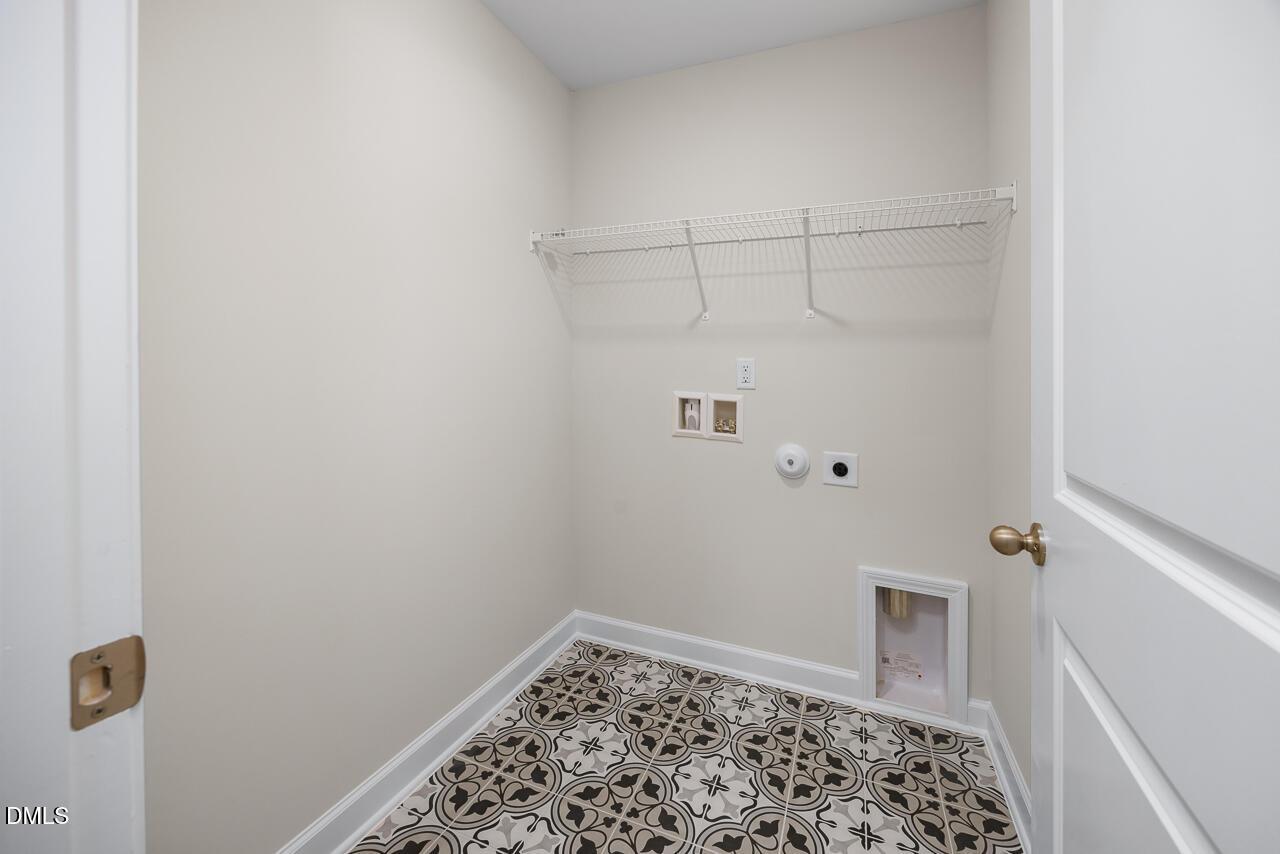 Spacious laundry room featuring wire shelving, washer-dryer hookups, pet door, and patterned tile floor in Davidson Homes The Grace C, Lillington, NC