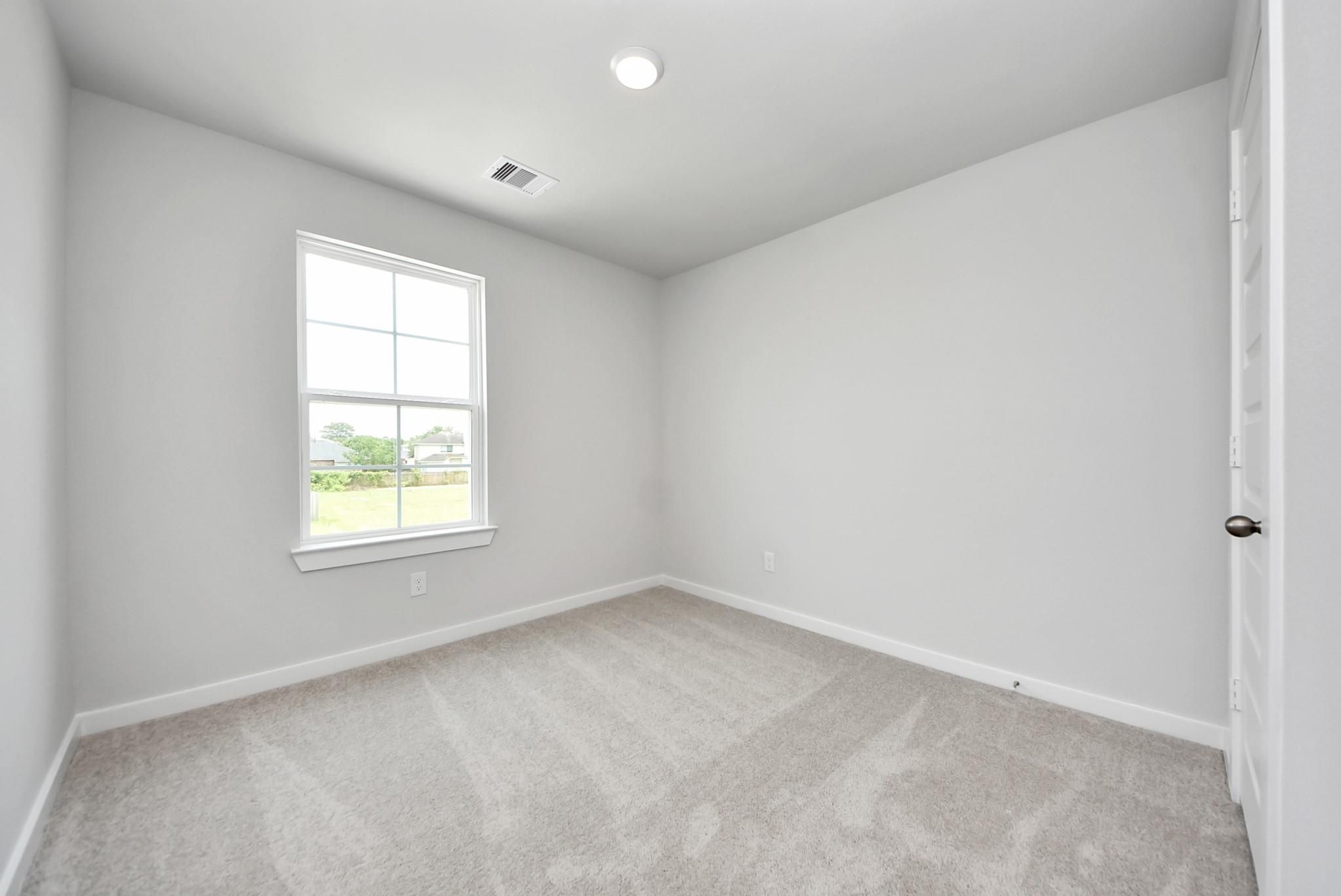 Bright, carpeted spare bedroom in The Blanco E floor plan at The Villages at WestPointe in Dayton, Texas.