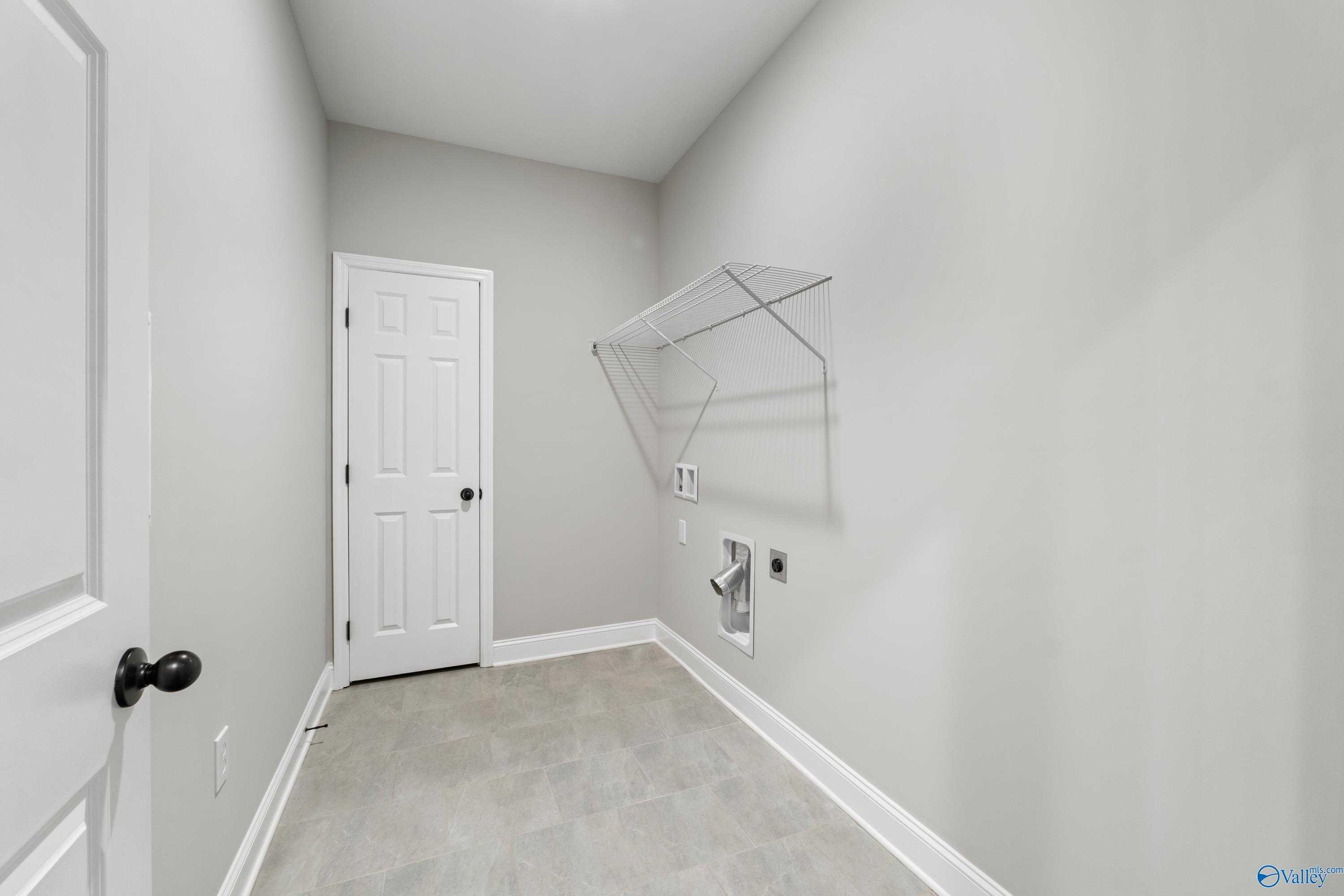 Modern laundry room with utility sink, washer/dryer hookups, open shelves, and gray walls in Davidson Homes The Valencia, Meridianville, Alabama