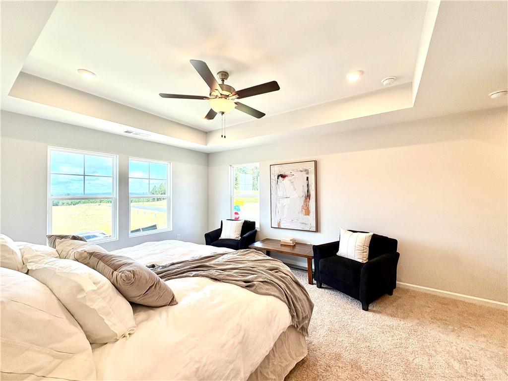 Serene master bedroom with king bed, tray ceiling, ceiling fan, armchairs, and field-view windows in Davidson Homes The Monroe A, Emerson, Georgia