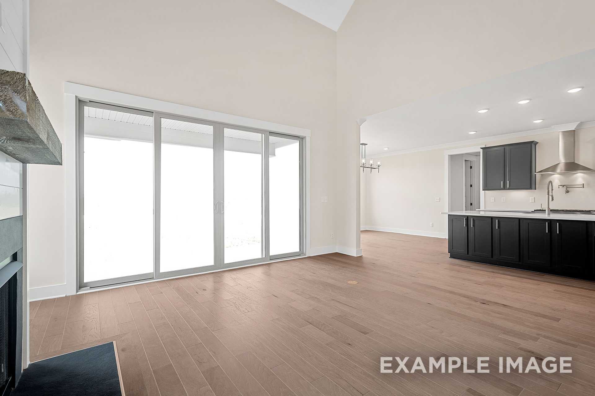 Spacious great room in The Hawkins with stone fireplace, sliding glass doors, open kitchen, black cabinets, hardwood floors