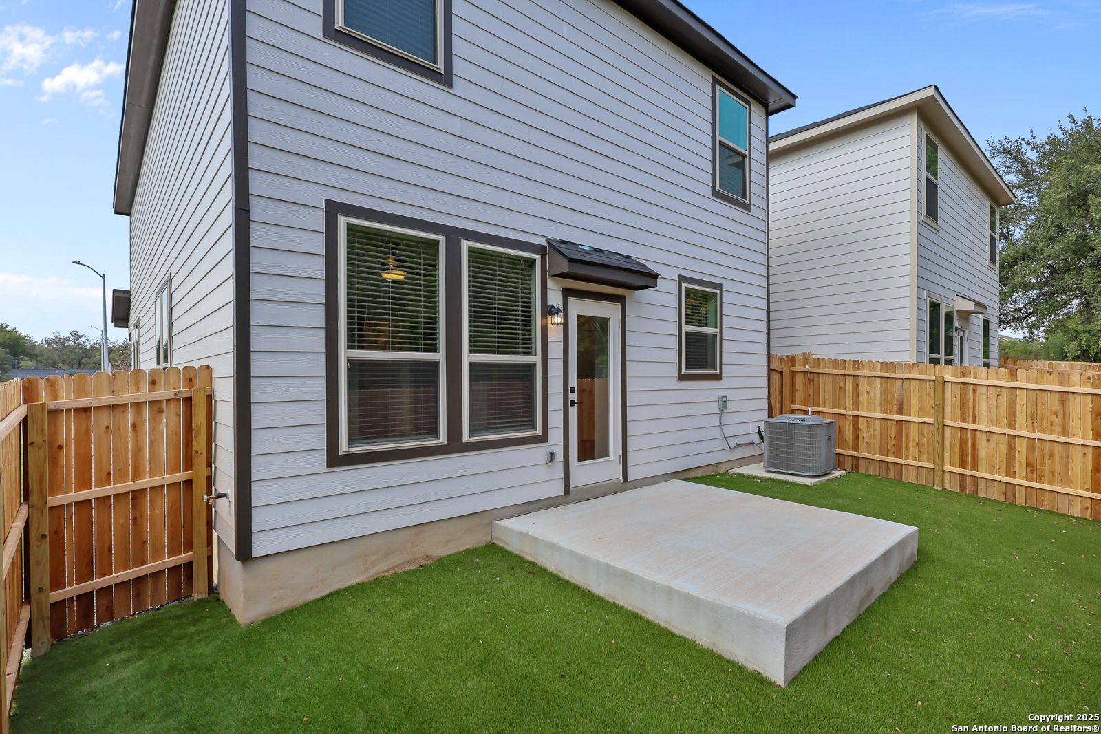 Private fenced backyard with lush green lawn, covered patio, and AC unit behind two-story Davidson Homes in Cedar Heights, San Antonio