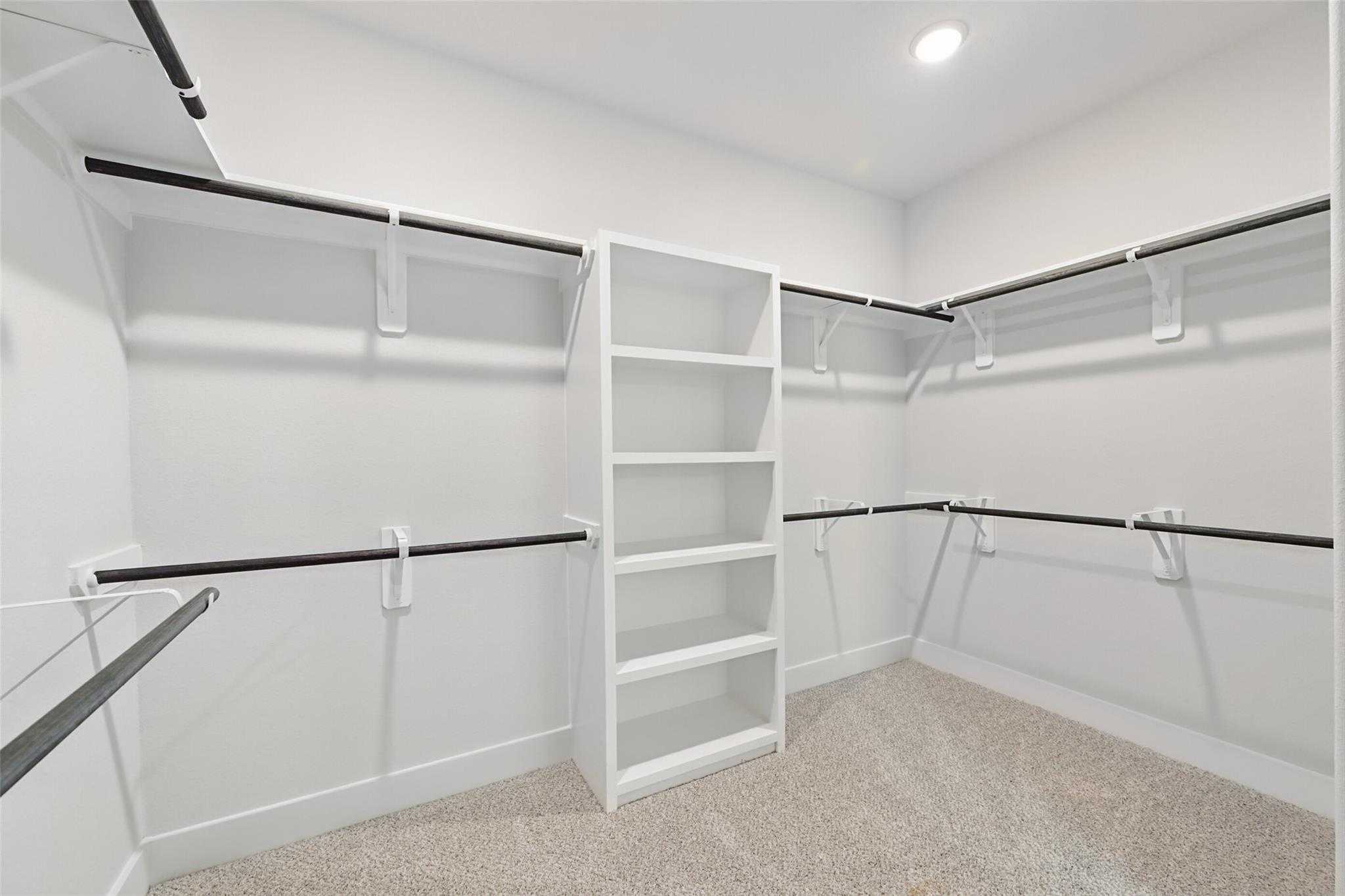 Spacious walk-in closet with white shelving, hanging rods, and beige carpet in Davidson Homes The Philip A, Lago Mar, Texas City