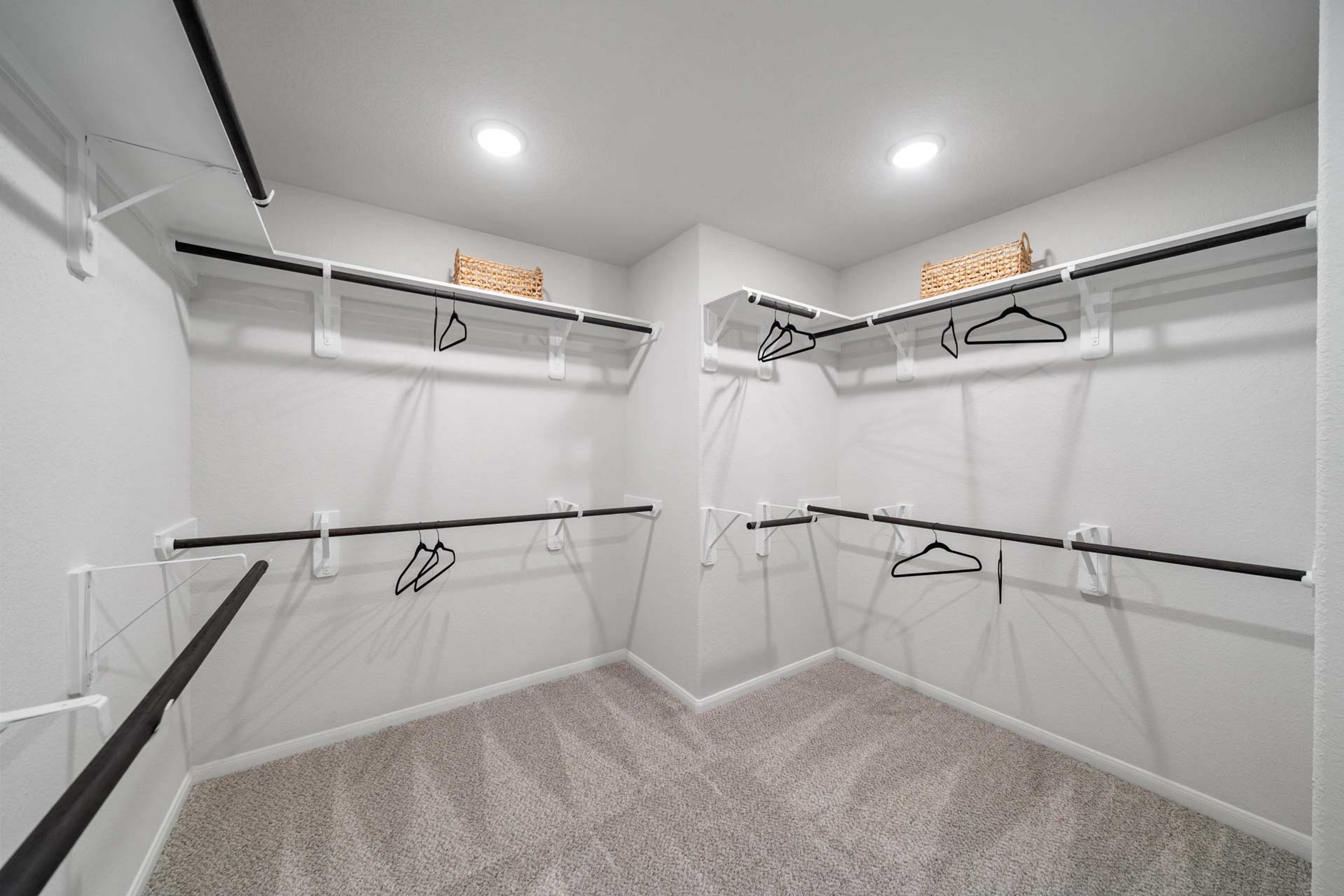Spacious corner walk-in closet with white shelving, black hanging rods, wicker baskets in Windmill Estates Magnolia TX home