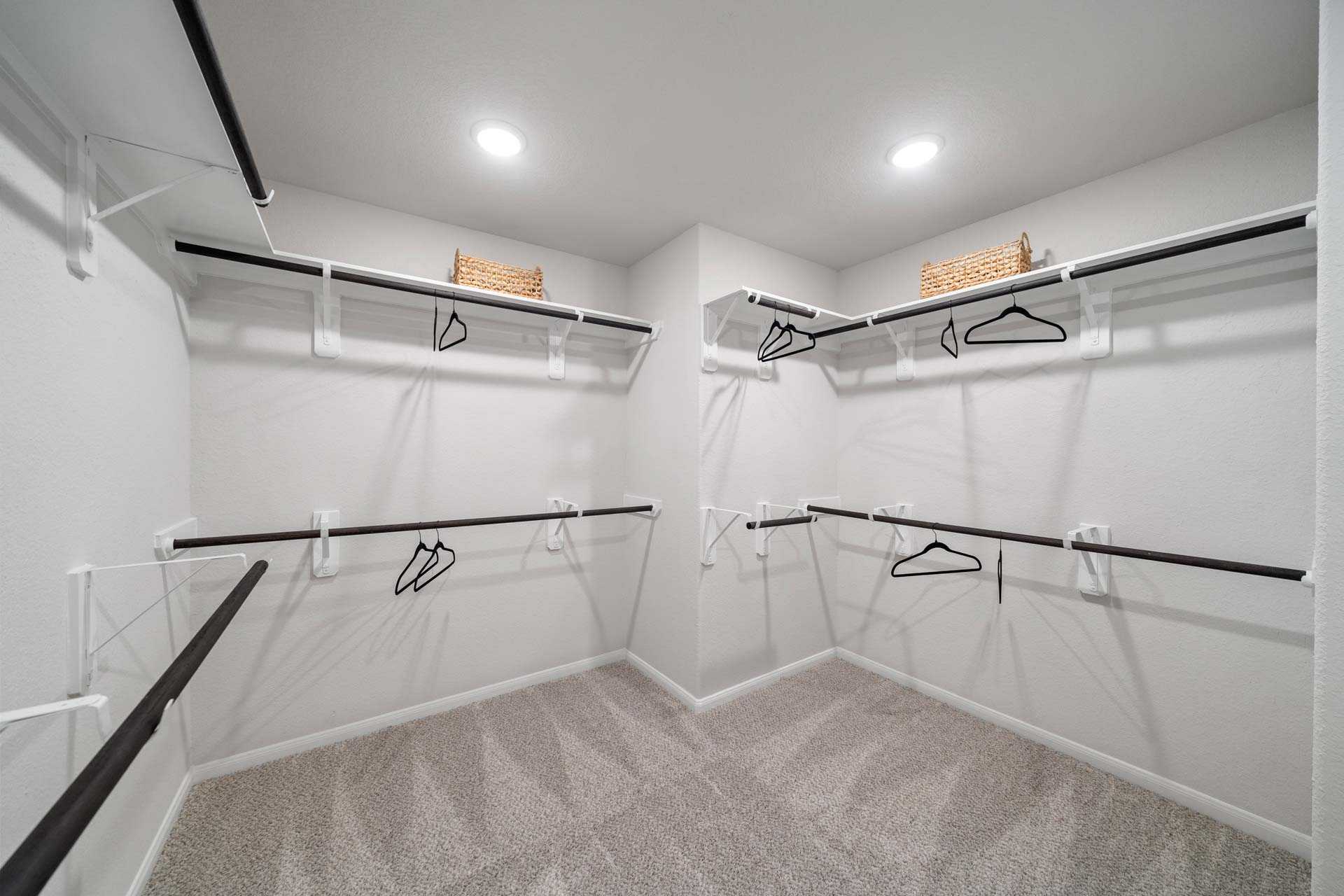 Spacious walk-in closet at Windmill Estates in Magnolia TX with black metal shelving, hanging rods, wicker baskets, and carpeted floor