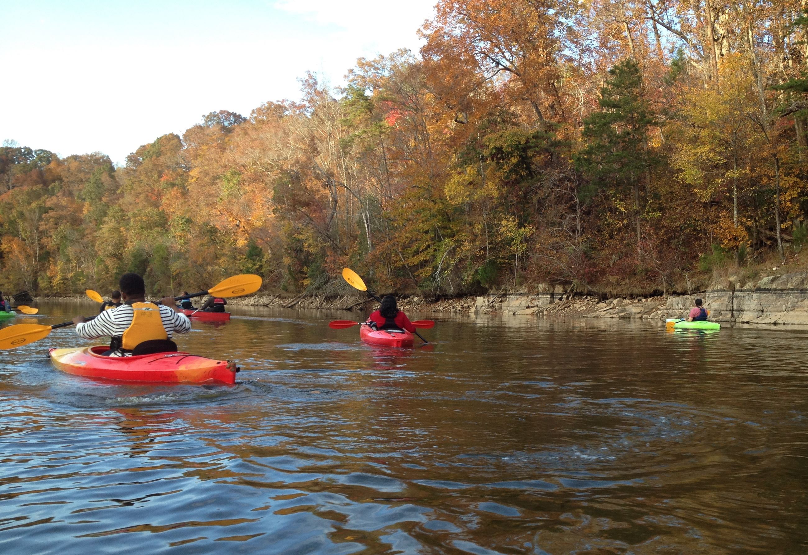 People kayaking on a river near Rockport in Wake Forest, NC, surrounded by vibrant autumn foliage.