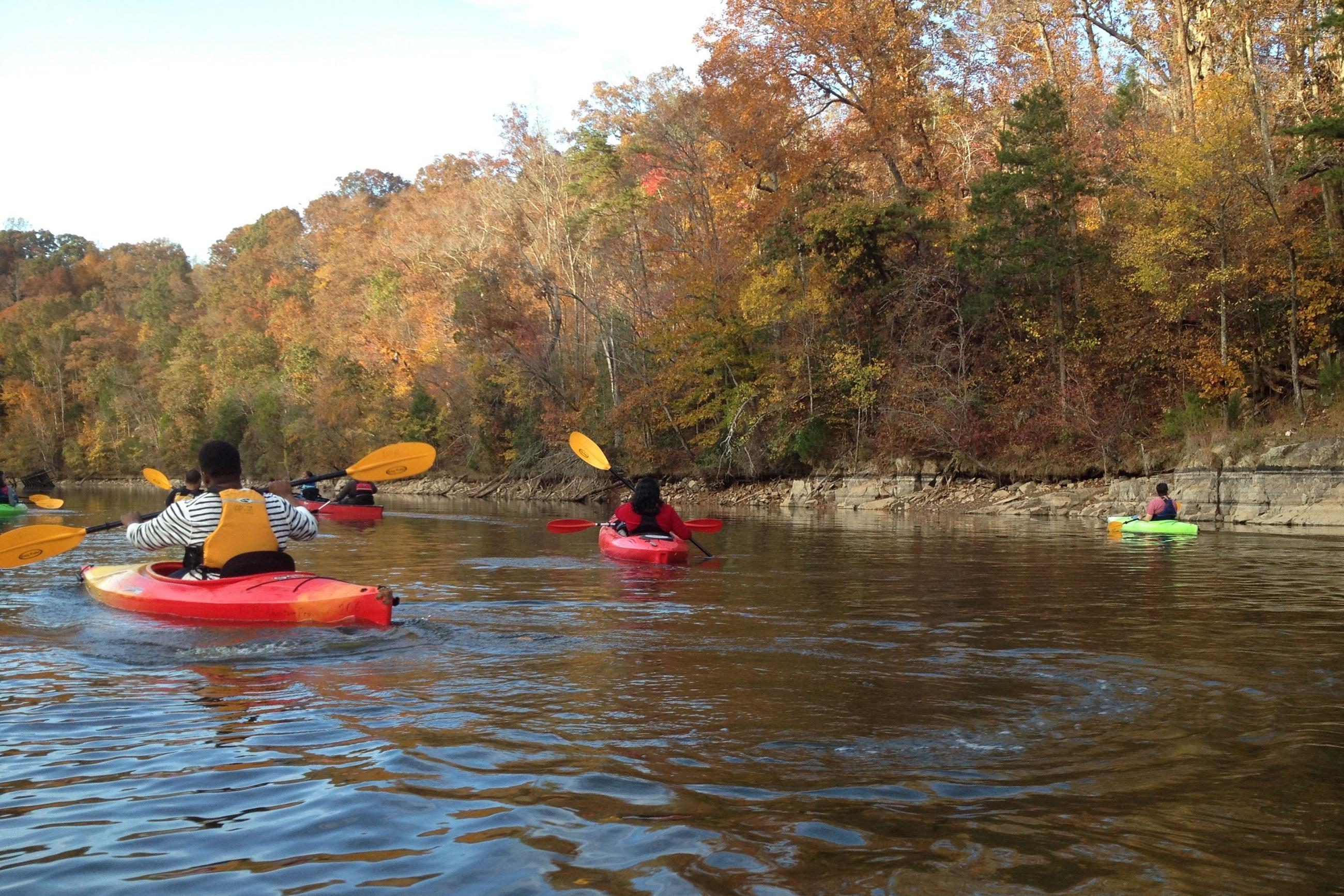 People kayaking on a river near Rockport in Wake Forest, NC, surrounded by vibrant autumn foliage.