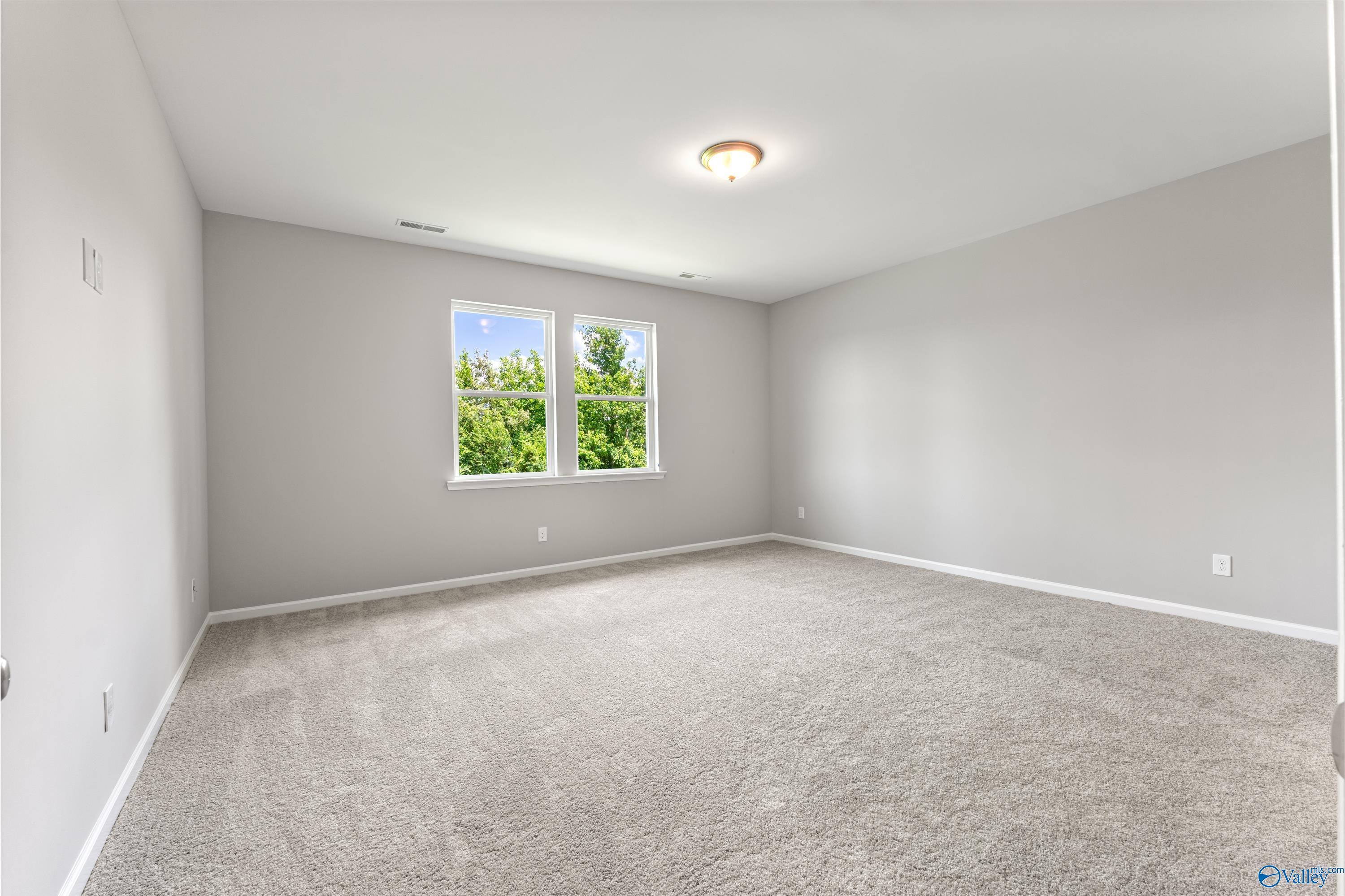 Bright secondary bedroom with gray walls, large sunny windows, and carpeted floor in Davidson Homes The Sanctuary, Huntsville, Alabama