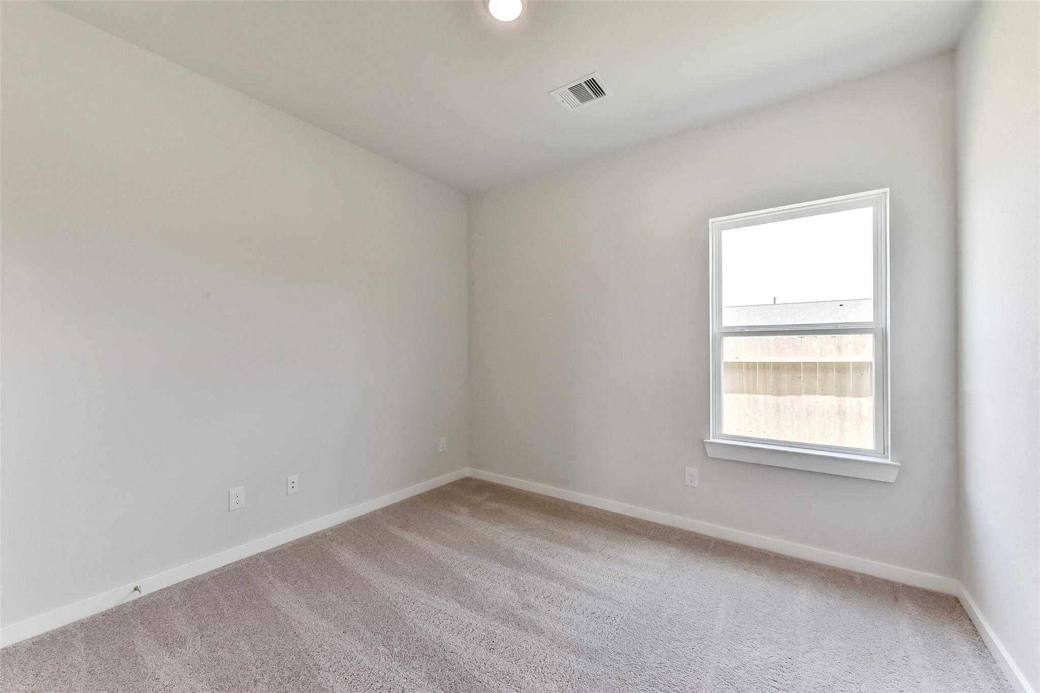Empty secondary bedroom featuring light gray walls, beige carpet, and large window in The Frio F by Davidson Homes, Dayton, Texas