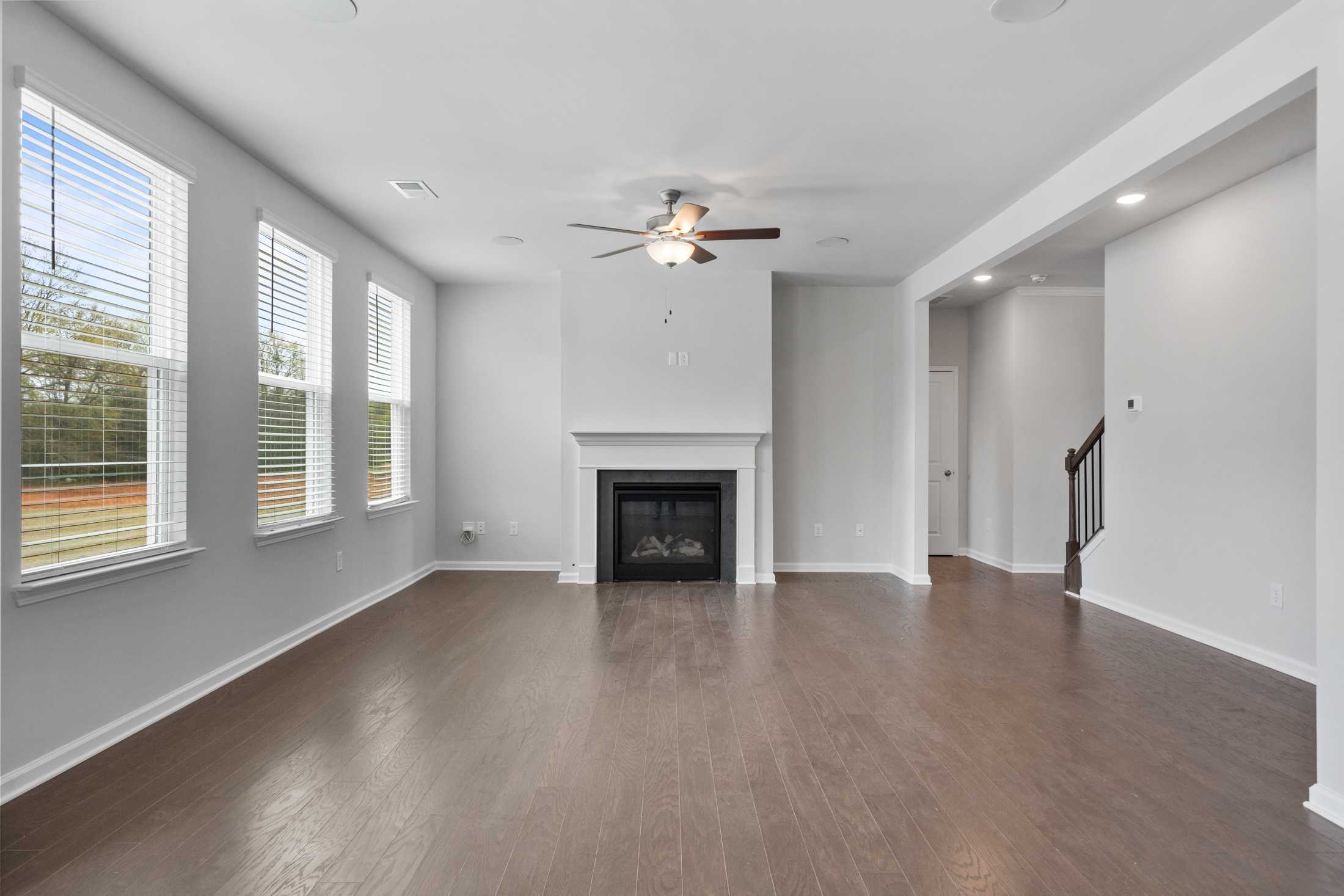 Open-concept living room at Reverie at East Lake in McDonough GA featuring hardwood floors, gas fireplace, and large windows