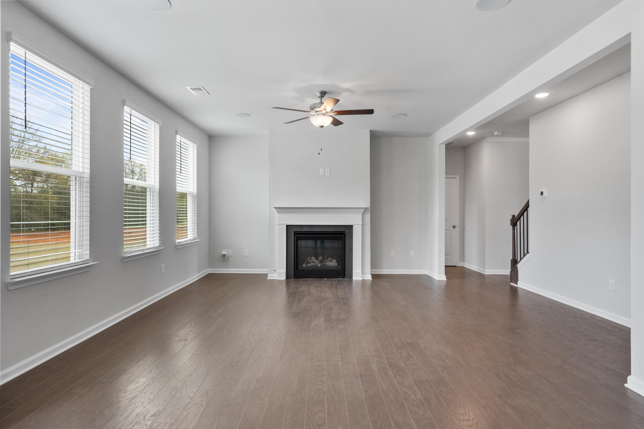 Open-concept living room at Reverie at East Lake in McDonough GA featuring hardwood floors, gas fireplace, and large windows
