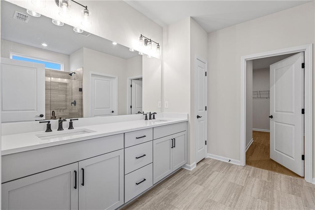 Modern master bathroom featuring double vanity, glass shower enclosure, and walk-in closet in Davidson Homes The Edison B, Loganville, GA