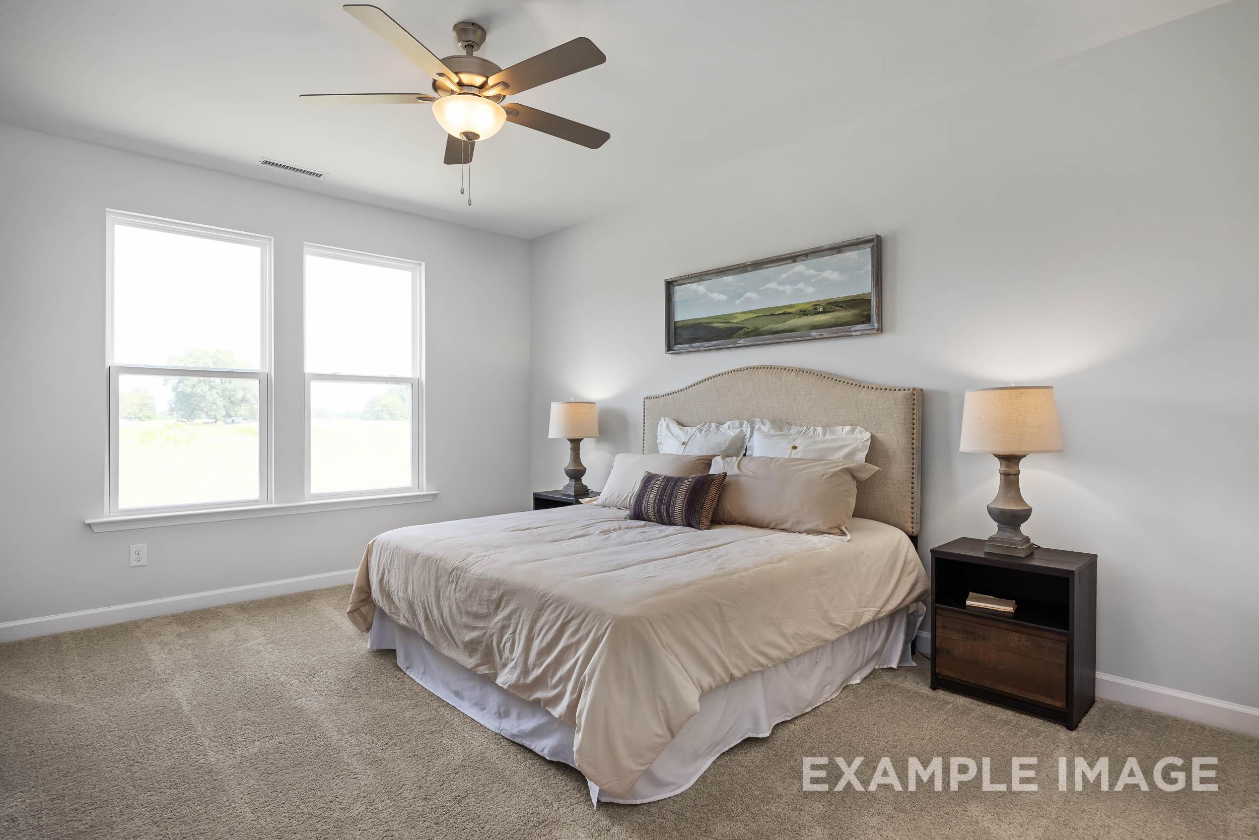 Spacious master bedroom in The Daphne C featuring king bed with neutral bedding, ceiling fan, lamps, and large windows