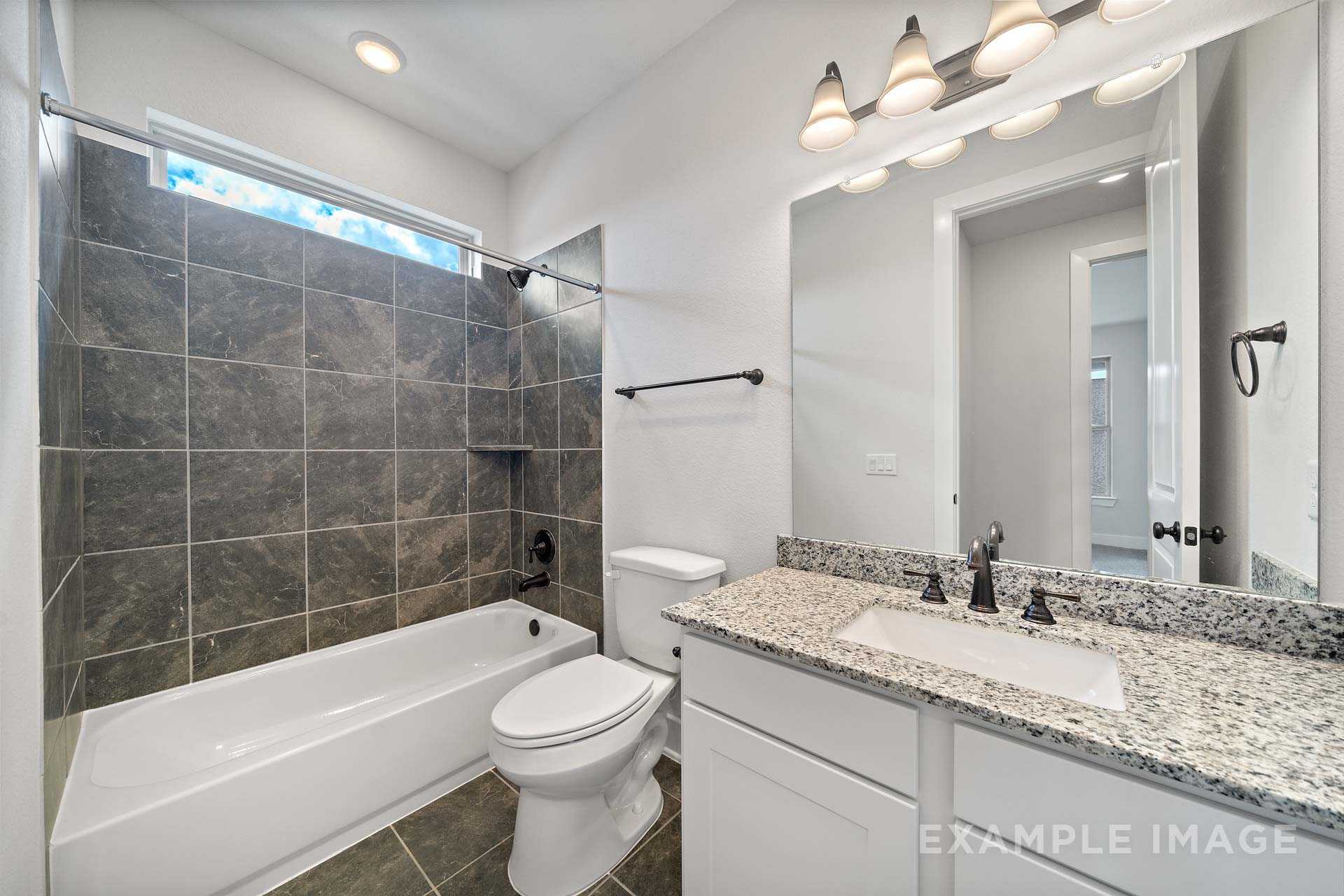 Luxurious master bathroom in The Victoria A featuring gray tiled shower, soaking tub, and granite vanity