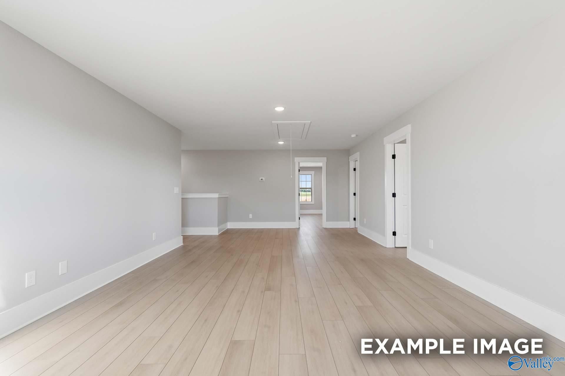 Spacious empty living room with light oak hardwood floors, gray walls, bar counter in The Emory 4-bedroom home, Decatur, Alabama