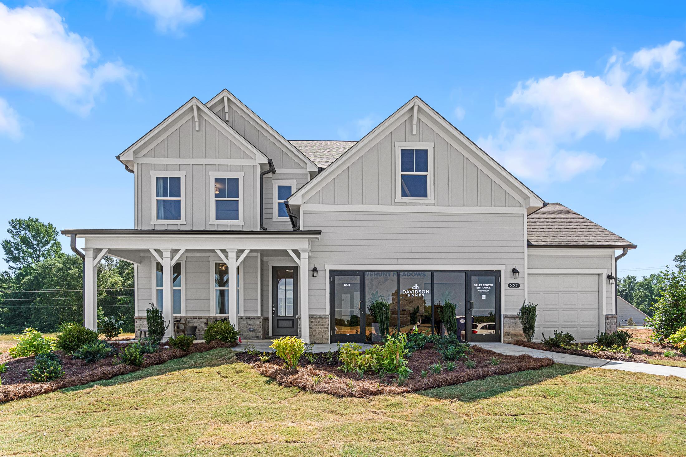 Two-story Hickory B craftsman home at Wehunt Meadows with gray siding, wrap-around porch, two-car garage, and lush landscaping in Hoschton GA