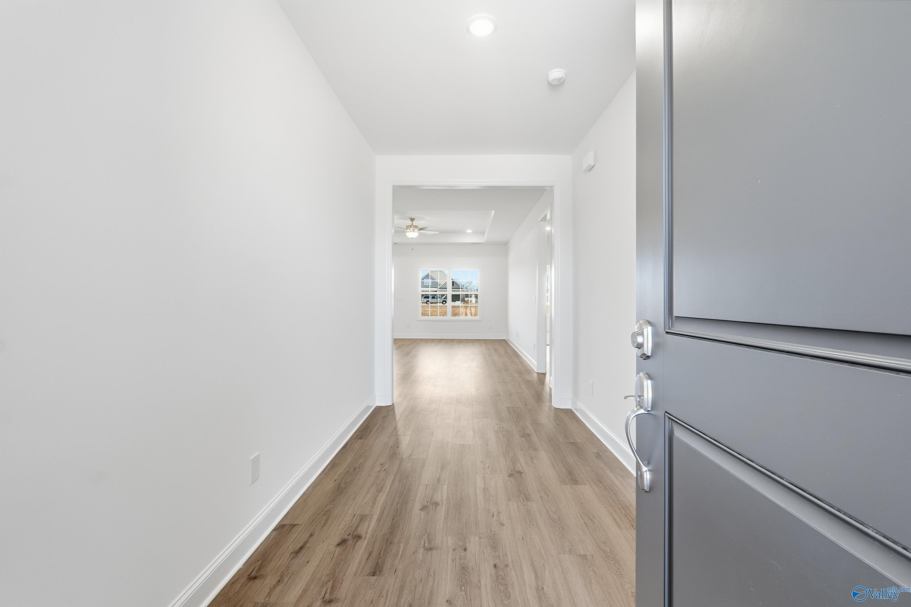 Bright hallway with hardwood floors, white walls, and open doorway in The Montgomery 3-bedroom home, Meridianville, Alabama