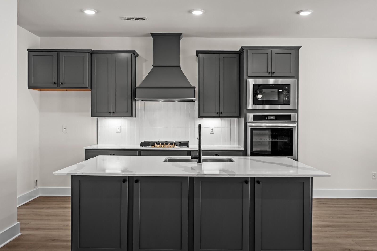 Modern kitchen with dark gray cabinets, white quartz island, and stainless appliances in The Willow at Woods Crossing, Gallatin.